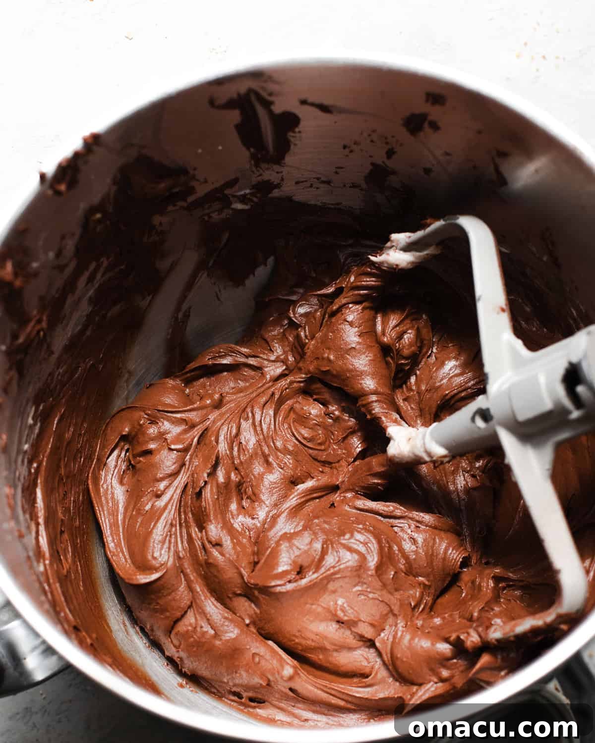 Decadent chocolate cream cheese frosting is shown in the bowl of a stand mixer, perfectly whipped to a smooth, creamy consistency, ready for cake assembly.