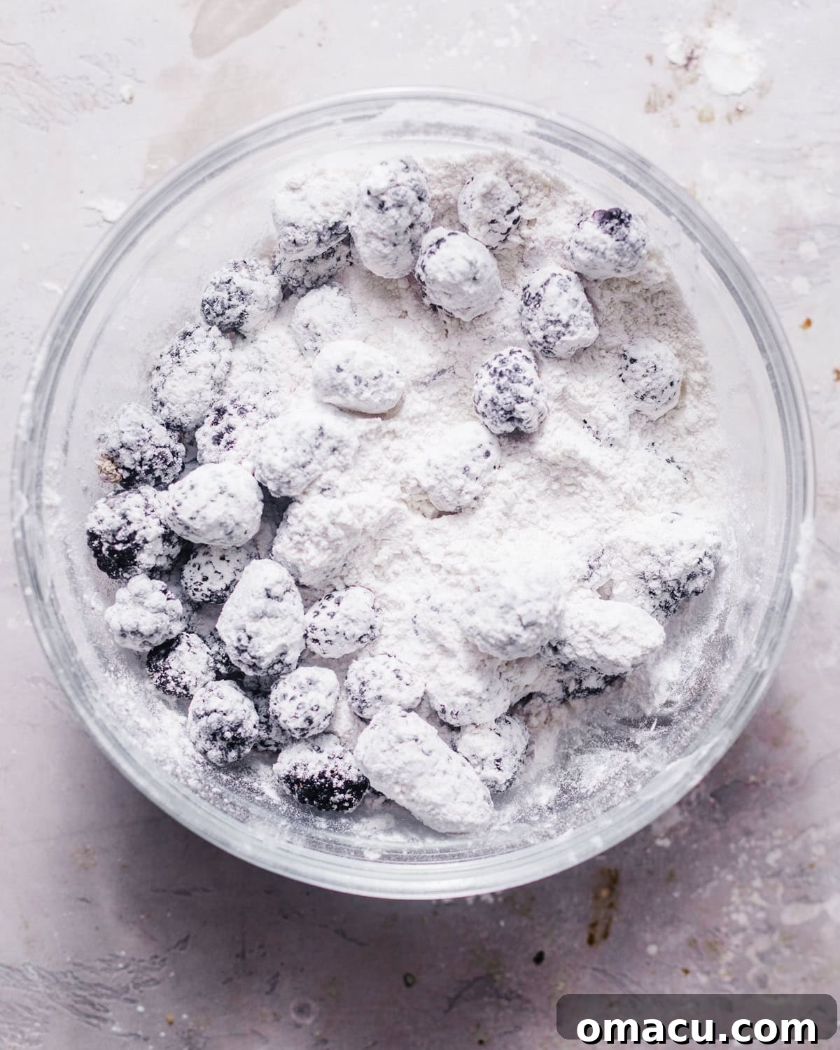 Dry ingredients and fresh blackberries tossed together in a bowl, lightly coated with flour.