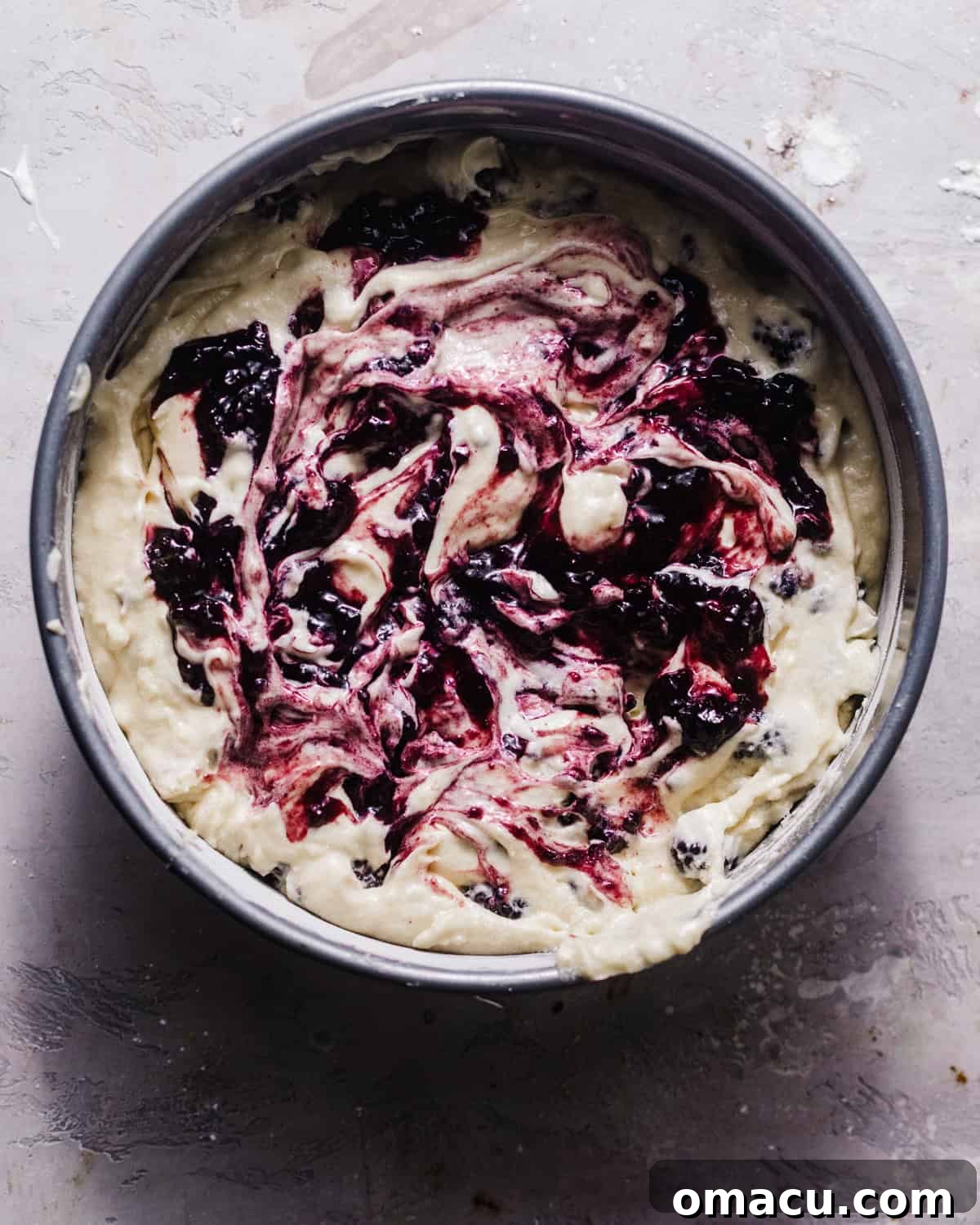 Coffee cake batter in a springform pan with dollops of blackberry preserves swirled on top.