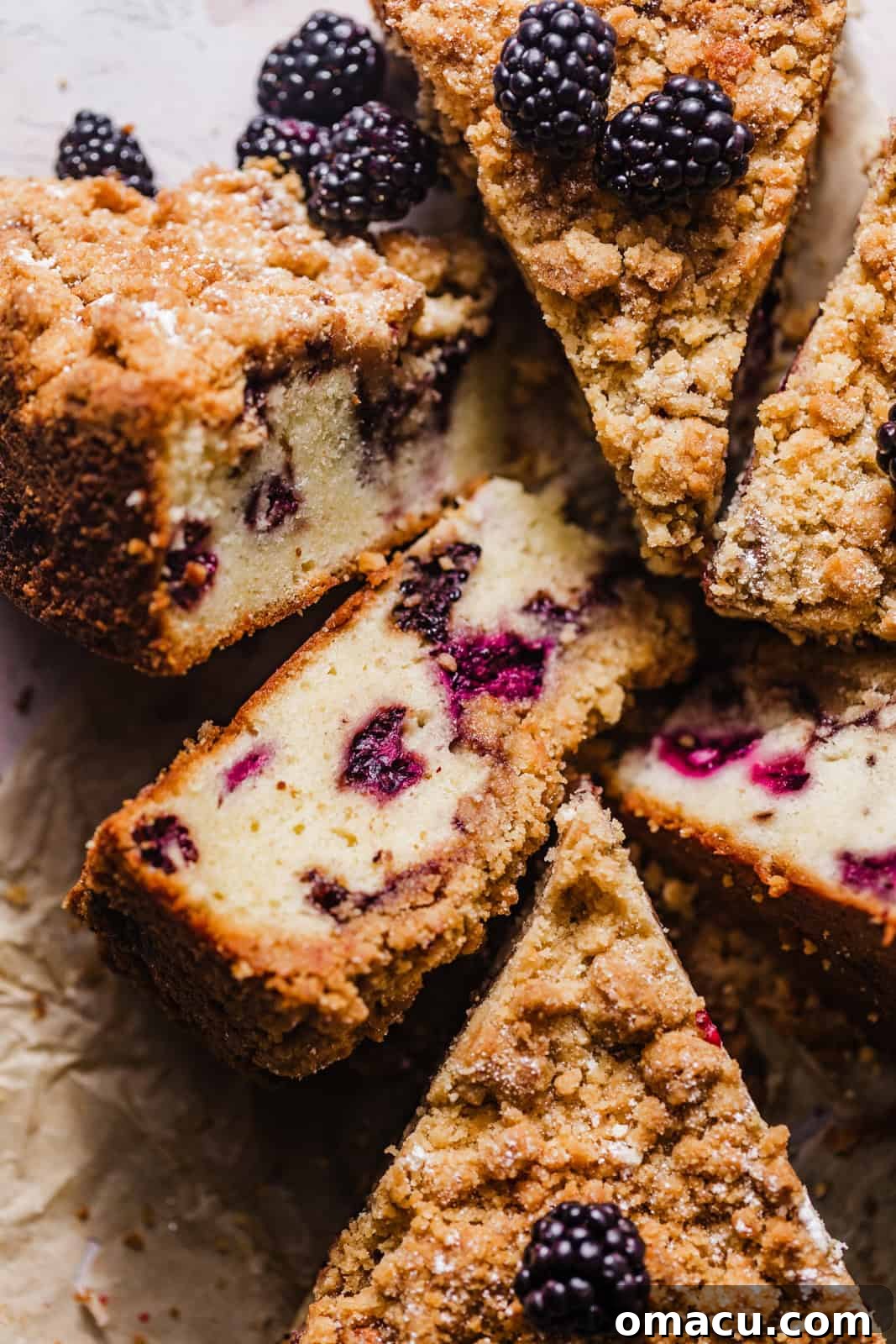 Sliced blackberry coffee cake on a piece of parchment paper, highlighting its moist crumb and berry distribution.