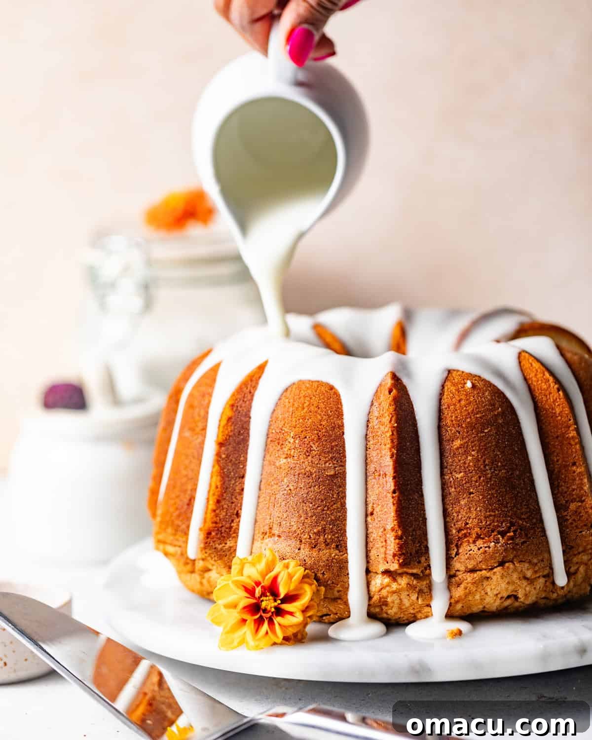 A perfectly glazed 7 Flavor Pound Cake on a elegant cake plate with a rich, white glaze being drizzled on top, showcasing its moist texture.