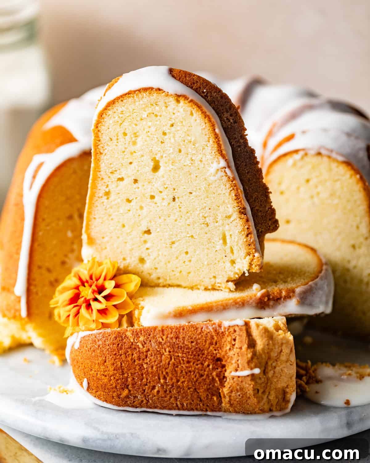 An inviting close-up photo of a generous slice of 7 flavor pound cake, placed on a white plate, with more slices stacked behind it, showcasing its perfect crumb.