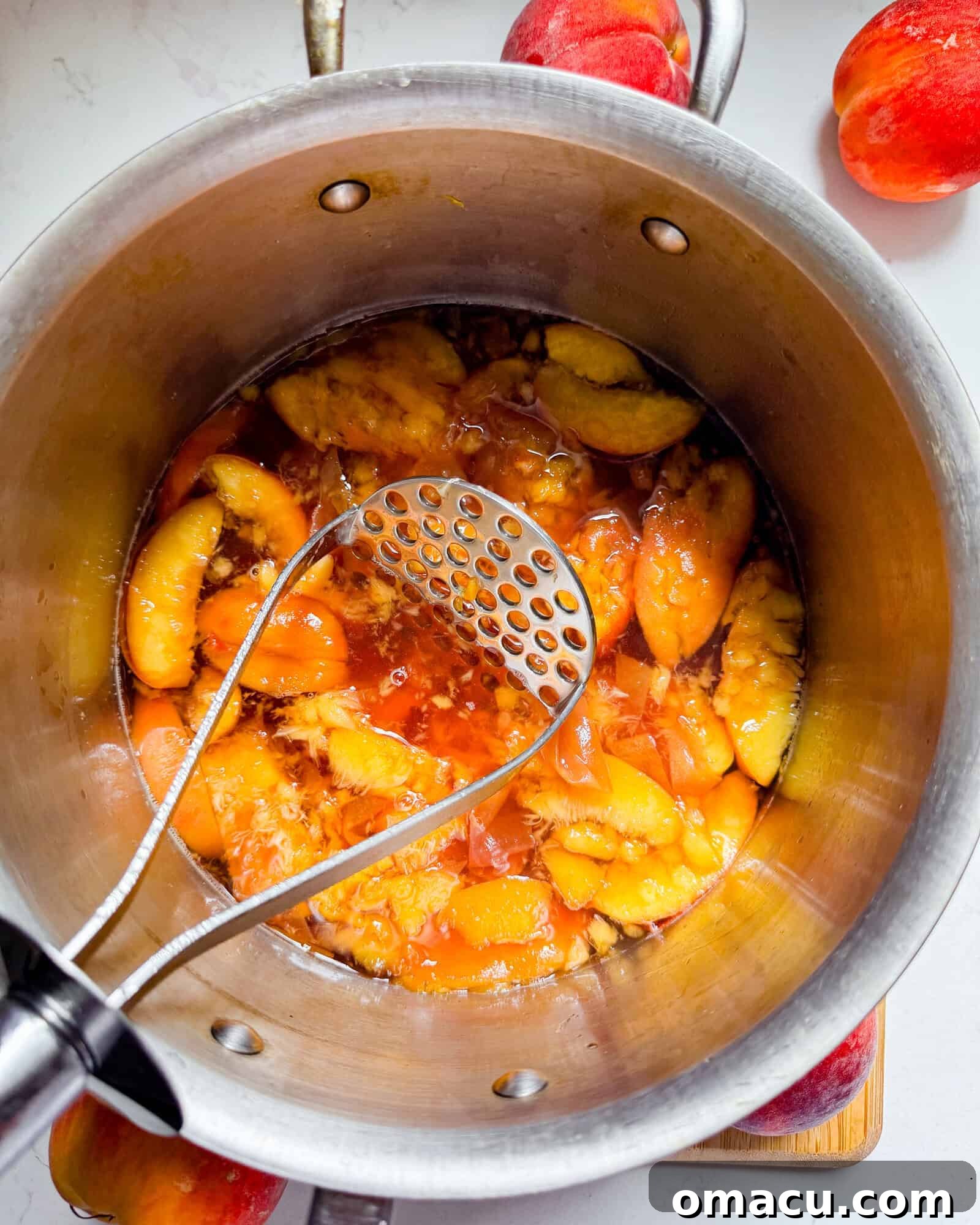 Mashed peaches in a saucepan, releasing their juice and flavor into the simmering syrup.