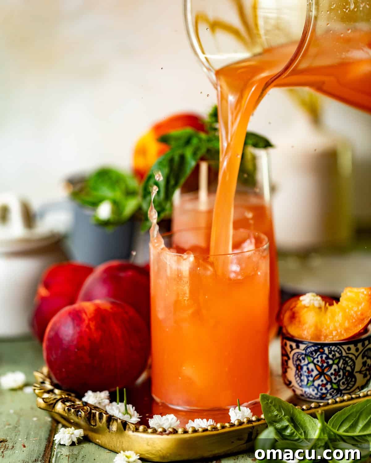 Homemade peach lemonade being poured from a pitcher into a glass filled with ice and garnished.