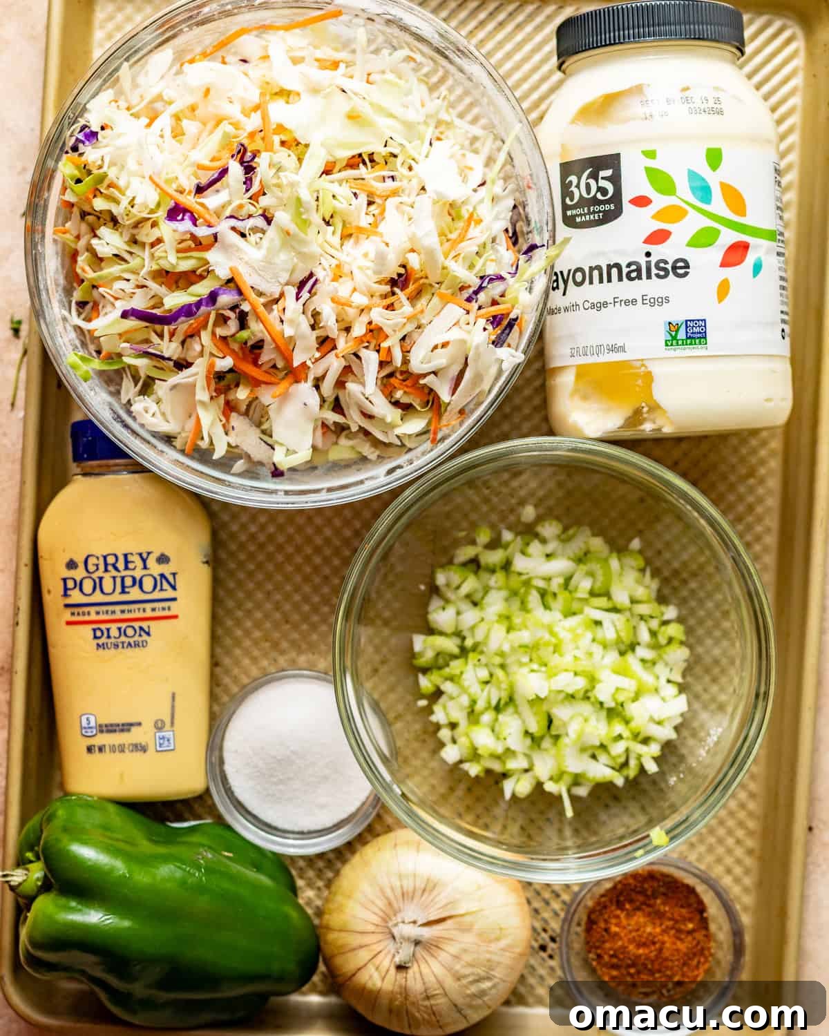 Assorted fresh ingredients laid out for making Cajun coleslaw, including shredded cabbage mix, mayonnaise, Dijon mustard, celery, onion, green bell pepper, Cajun seasonings, sugar, vinegar, and celery seed.