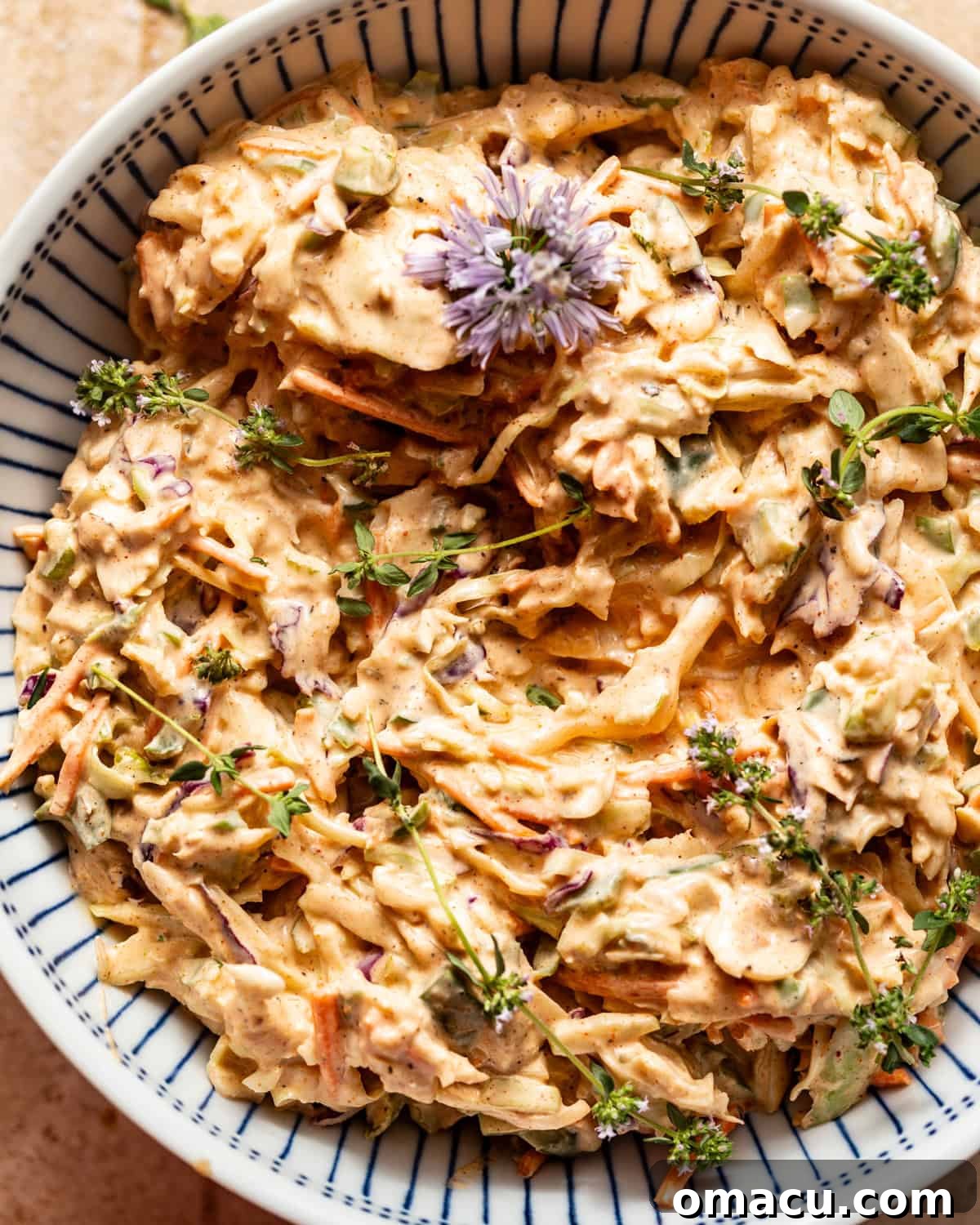 Close-up of Cajun coleslaw in a bowl, garnished with fresh chive flowers and thyme sprigs, ready for serving.