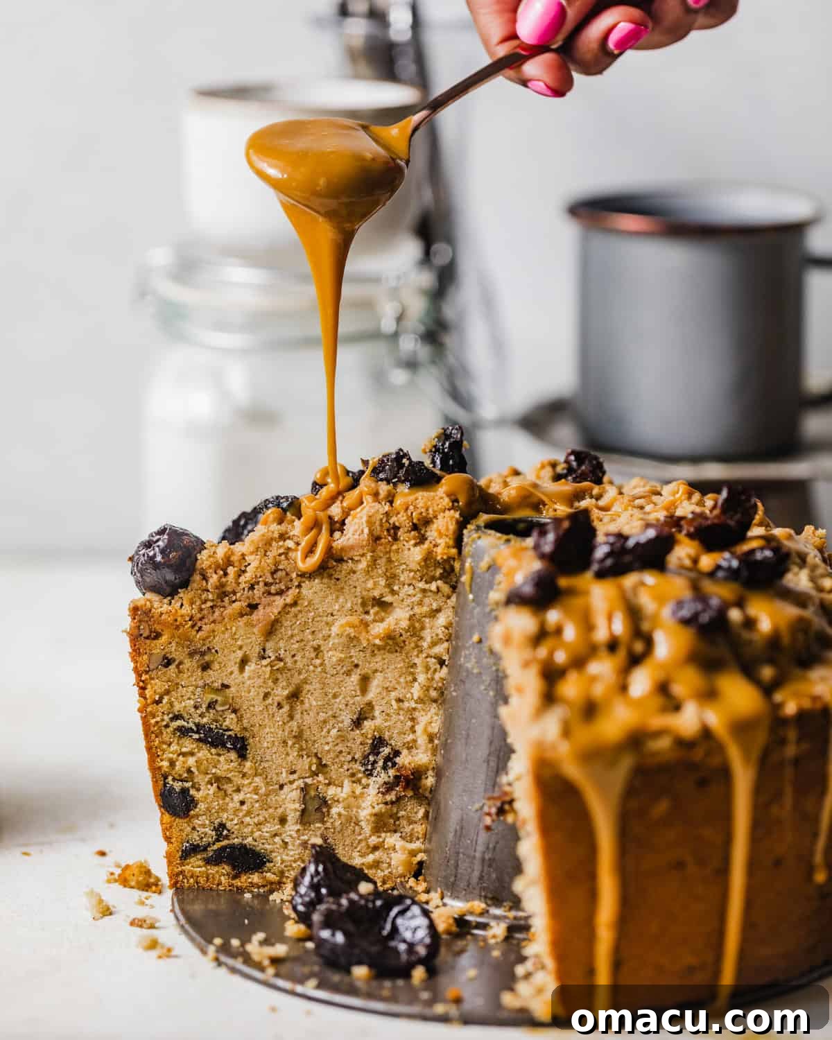 Vintage prune cake on a table with a spoon drizzling the dulce de leche glaze on top.