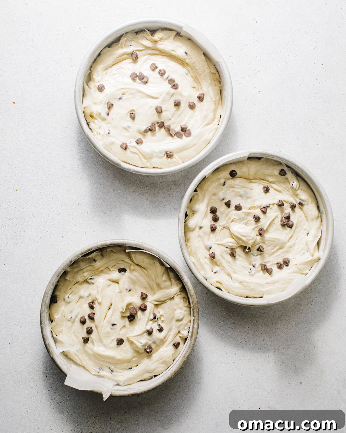 Evenly divided cake batter poured into three prepared cake pans, ready for baking.