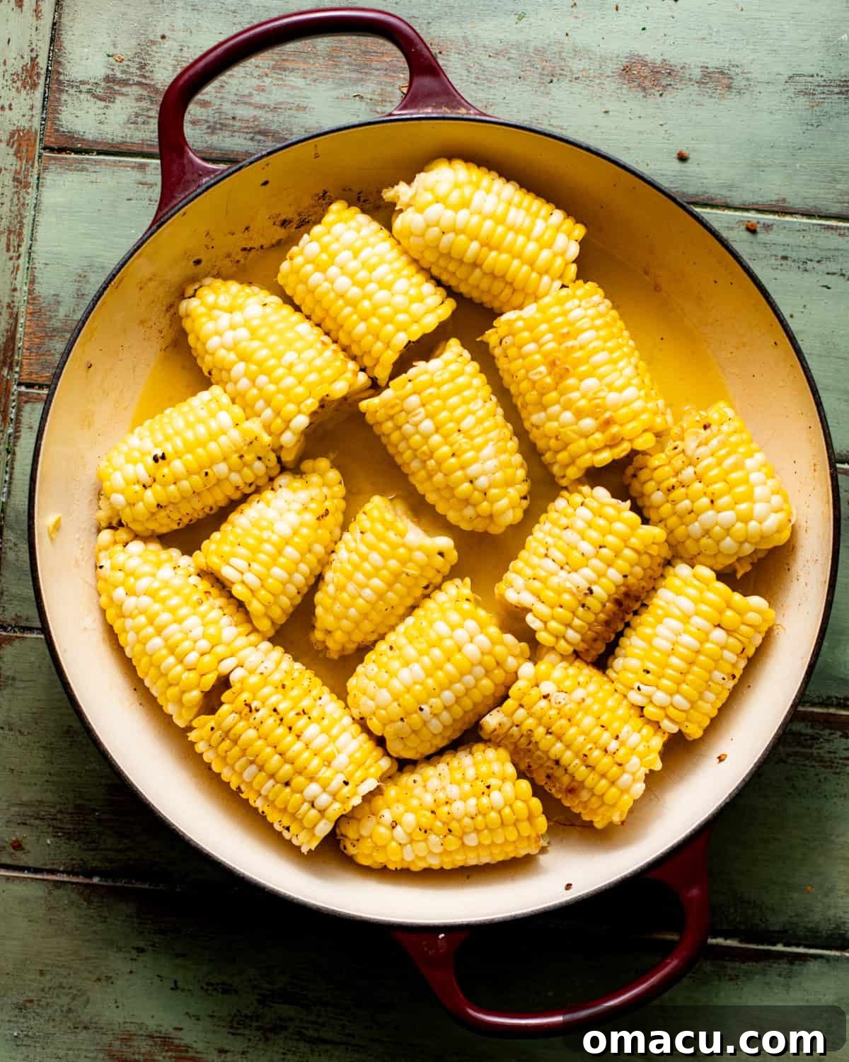 Corn on the cob pieces searing in a large pot with a lid nearby.