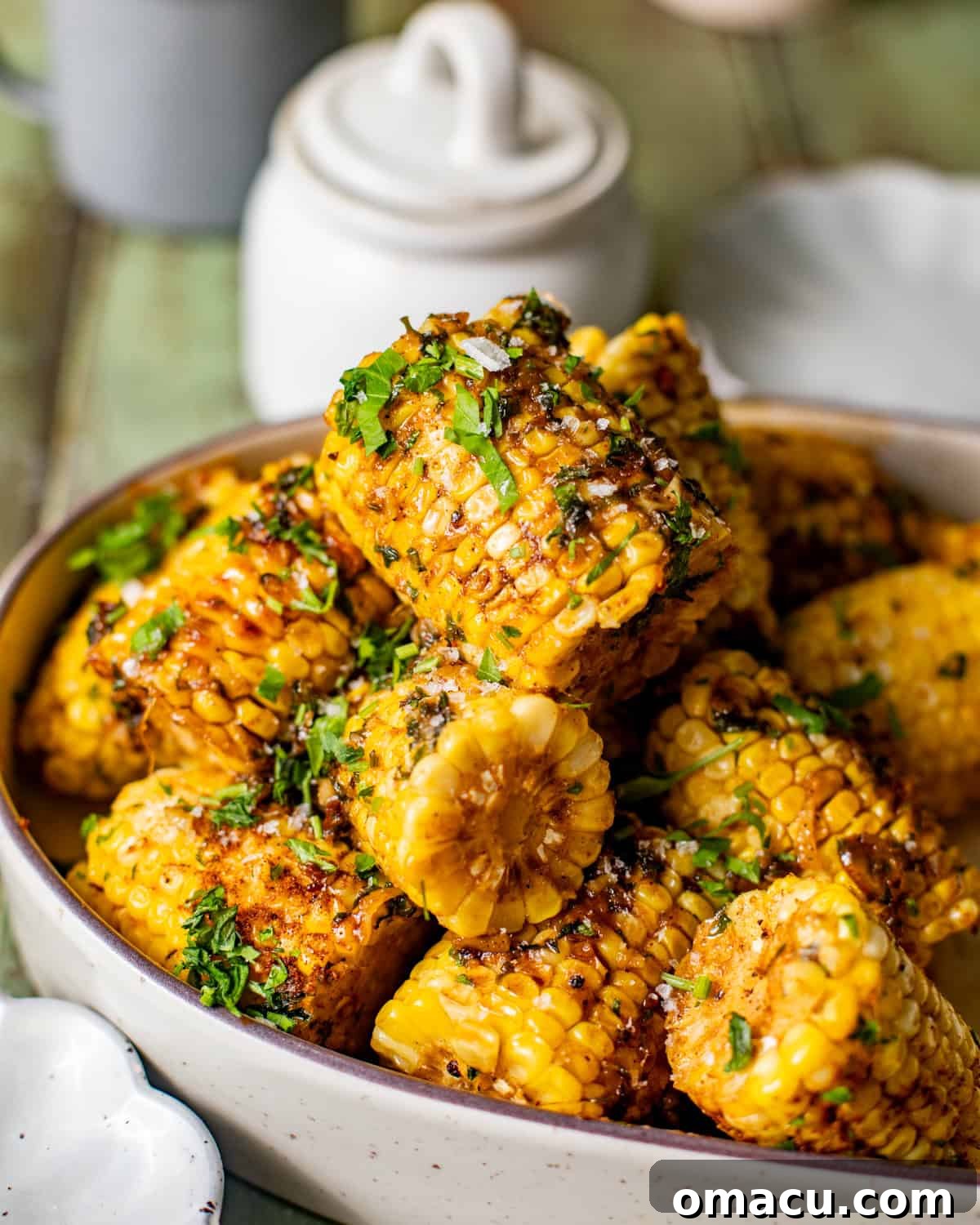 Serving bowl of Cajun corn on the cob covered in garlic butter, with a salt shaker in the background.