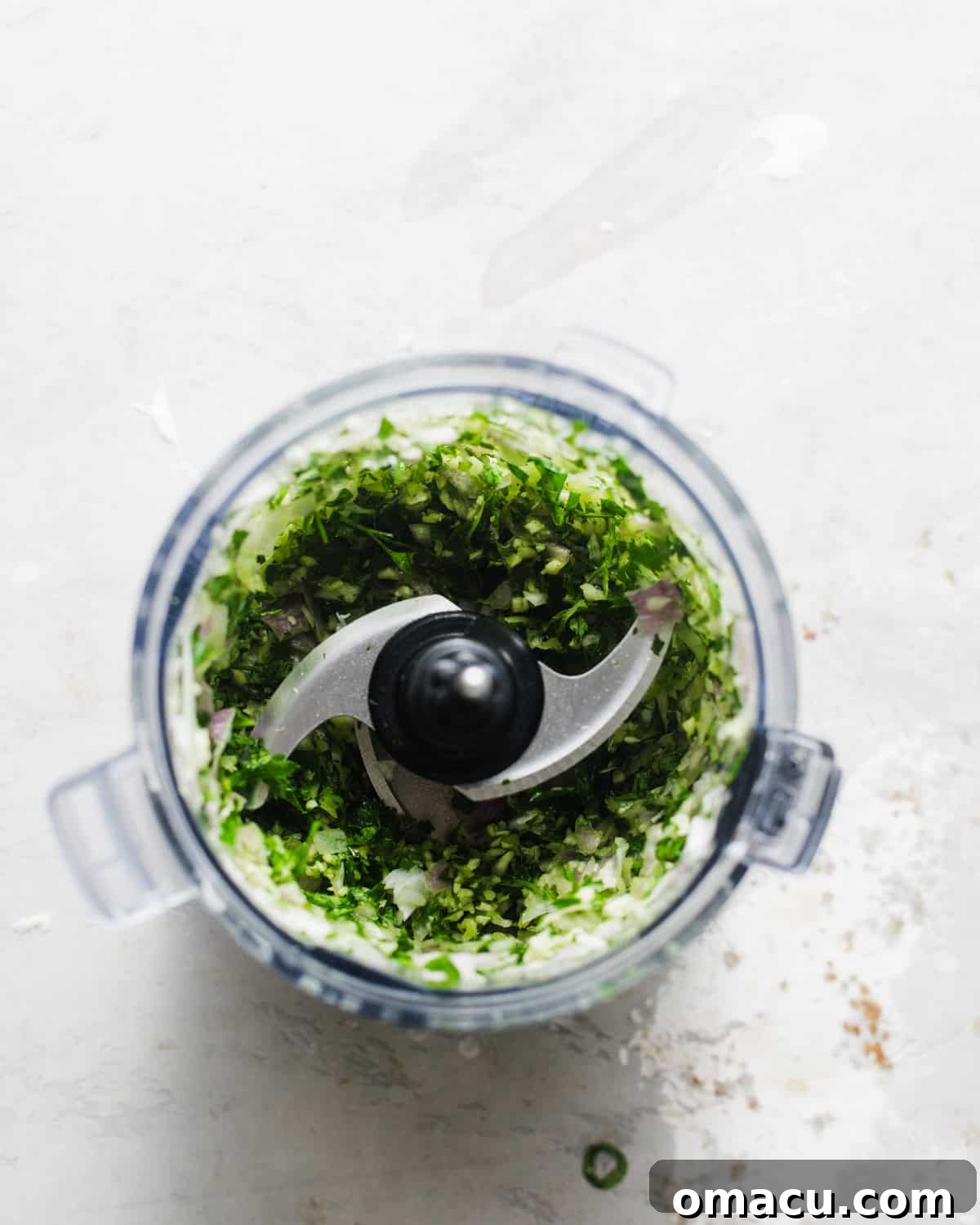 Fresh parsley, onion, shallot, and garlic being finely blended in a food processor, creating a vibrant green base for the chimichurri sauce.