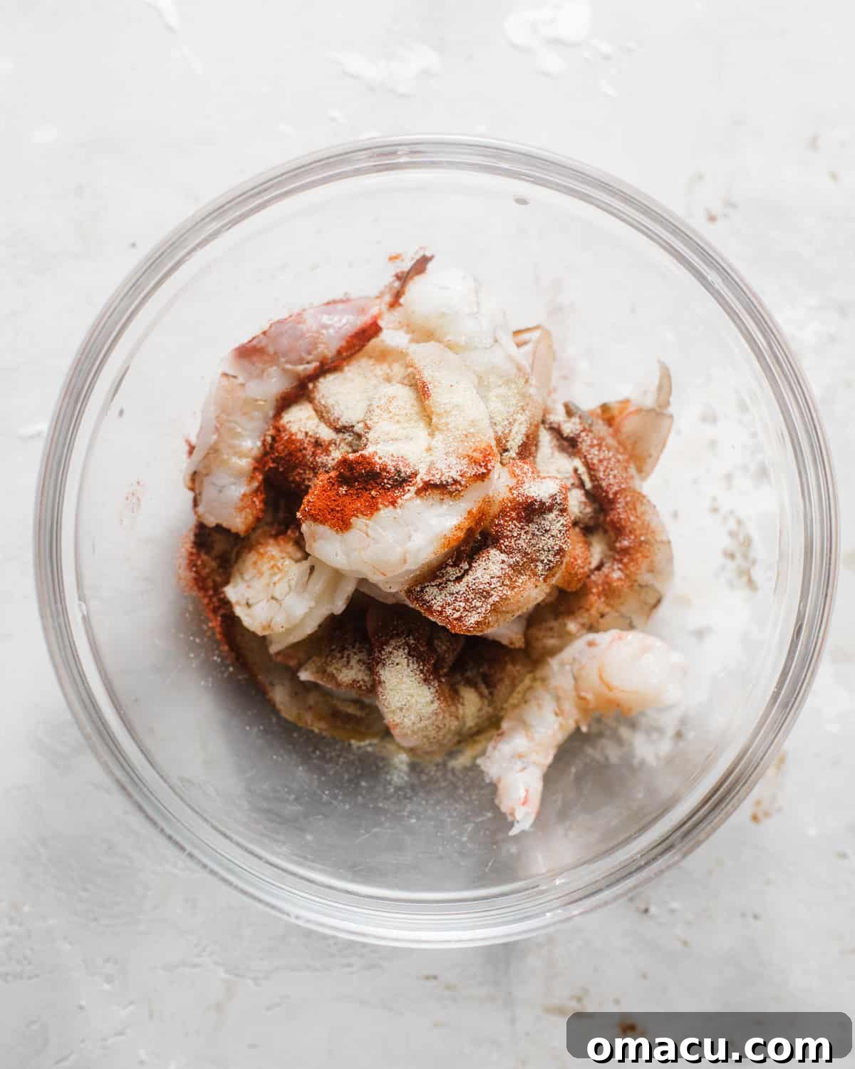 Plump shrimp, coated in a rich, orange-red seasoning blend, resting in a bowl, prepared for cooking.