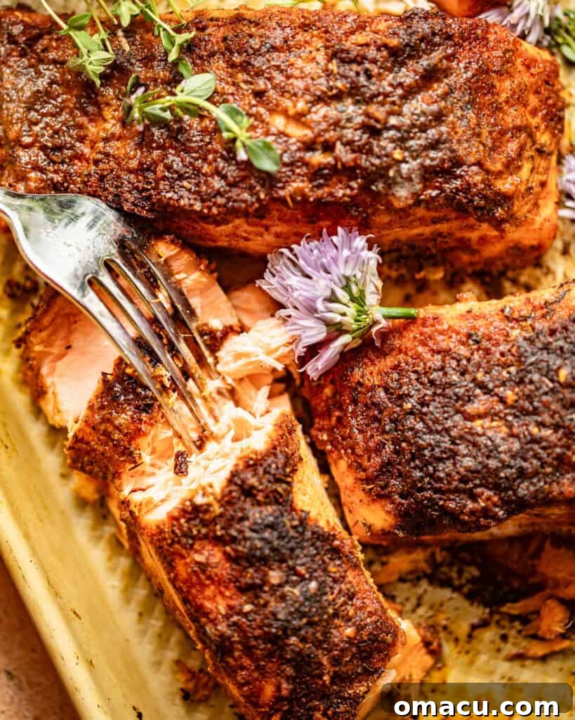 blackened baked salmon on a baking sheet with a fork, topped with fresh herbs.