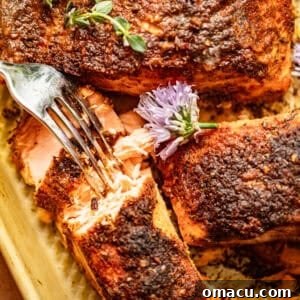 blackened baked salmon on a baking sheet with a fork, topped with fresh herbs.