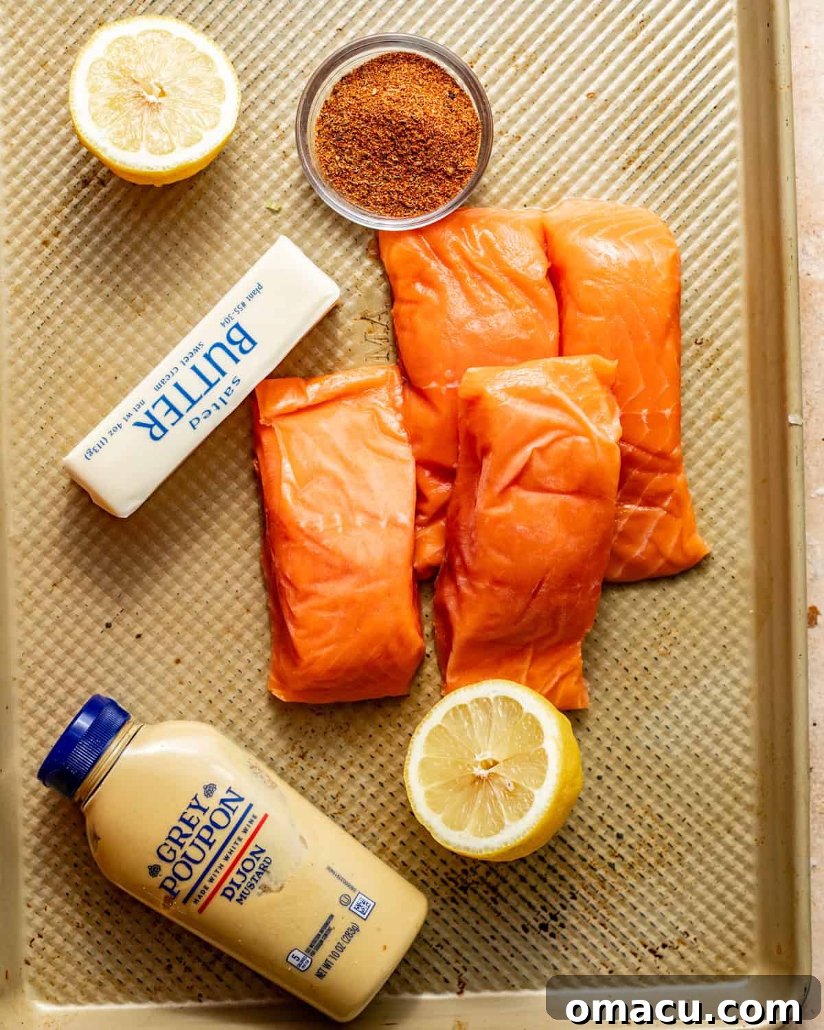 ingredients to make baked blackened salmon on a baking sheet - salmon filets, lemons, blackened seasoning, dijon mustard, butter, and honey. 