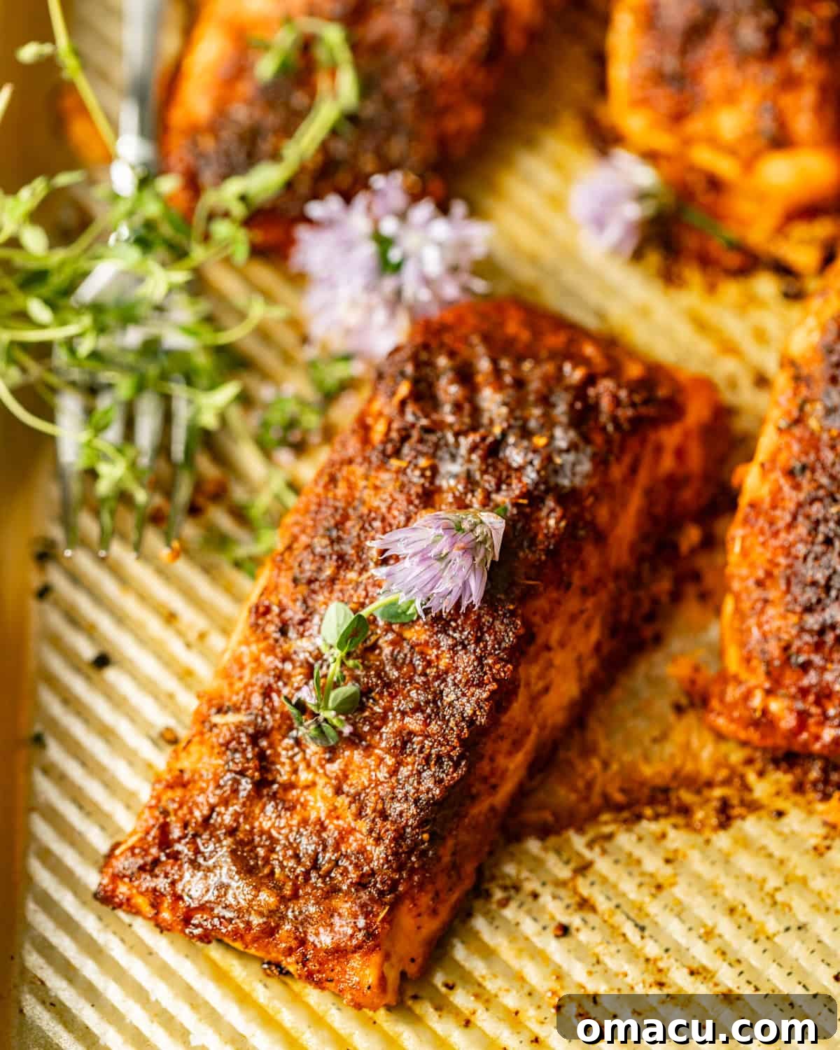 blackened baked salmon on a baking sheet with fresh herbs.