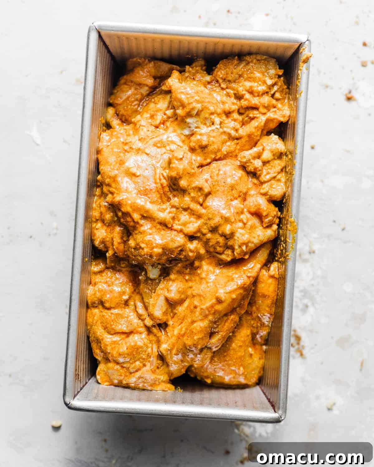Marinated chicken in a loaf pan, ready for baking to achieve a juicy and tender result.