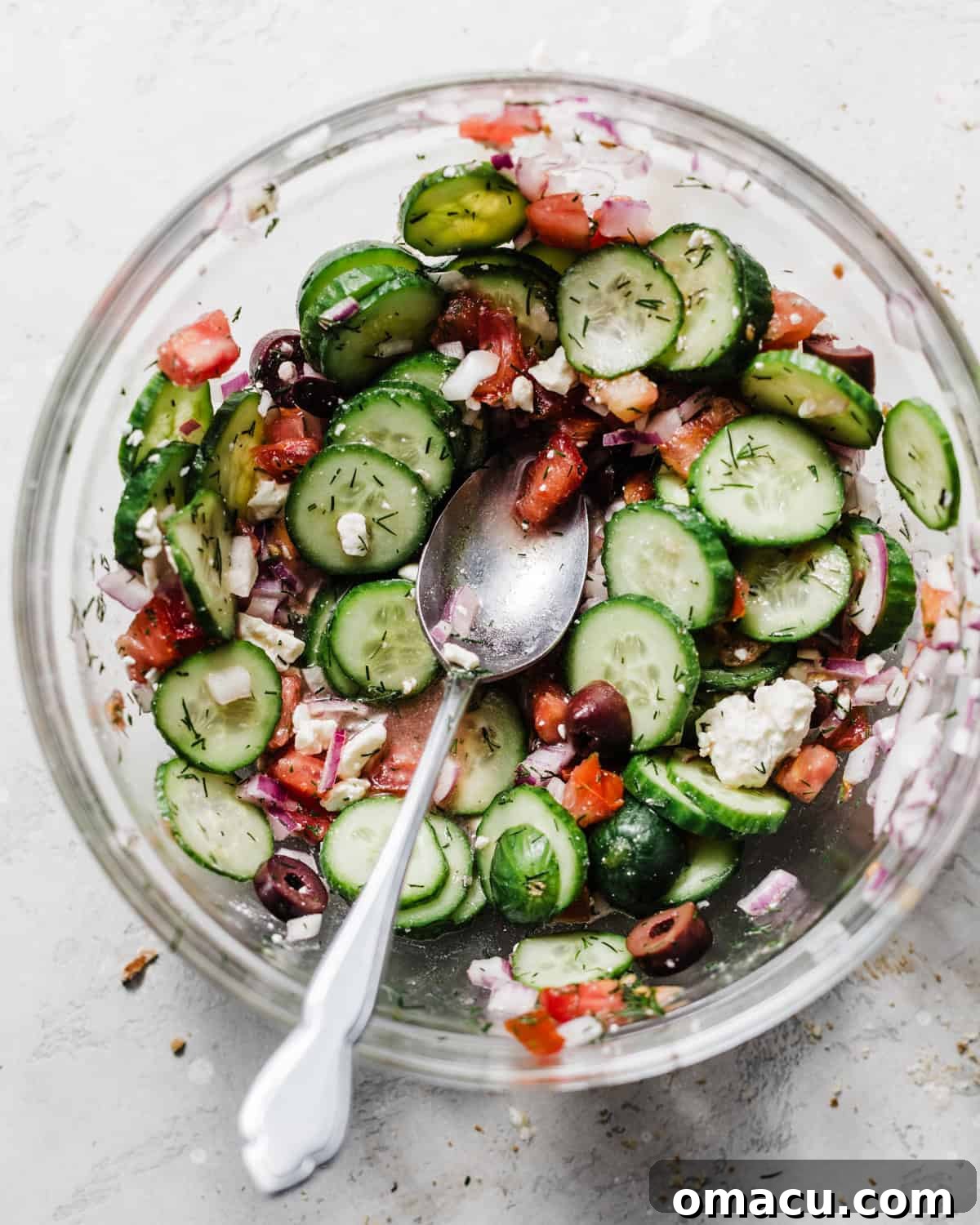 A crisp and colorful cucumber and tomato salad mixed together in a large bowl, featuring fresh dill and red onion.