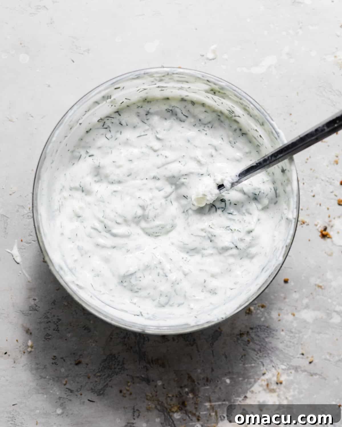 Creamy homemade Tzatziki sauce in a bowl with a spoon, garnished with fresh herbs, ready to be served.