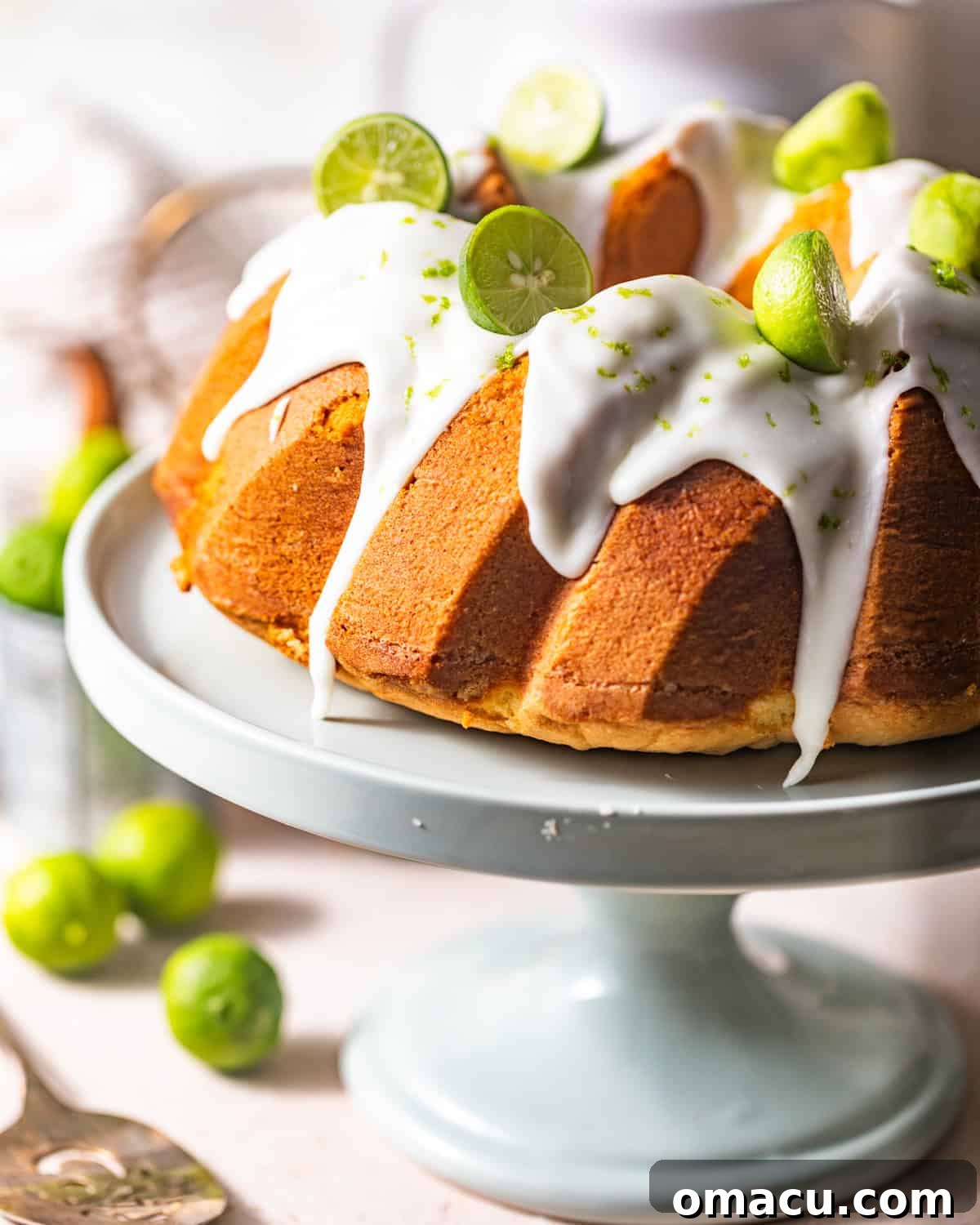 Key lime pound cake on a cake stand topped with key lime cream cheese glaze and fresh key lime zest.