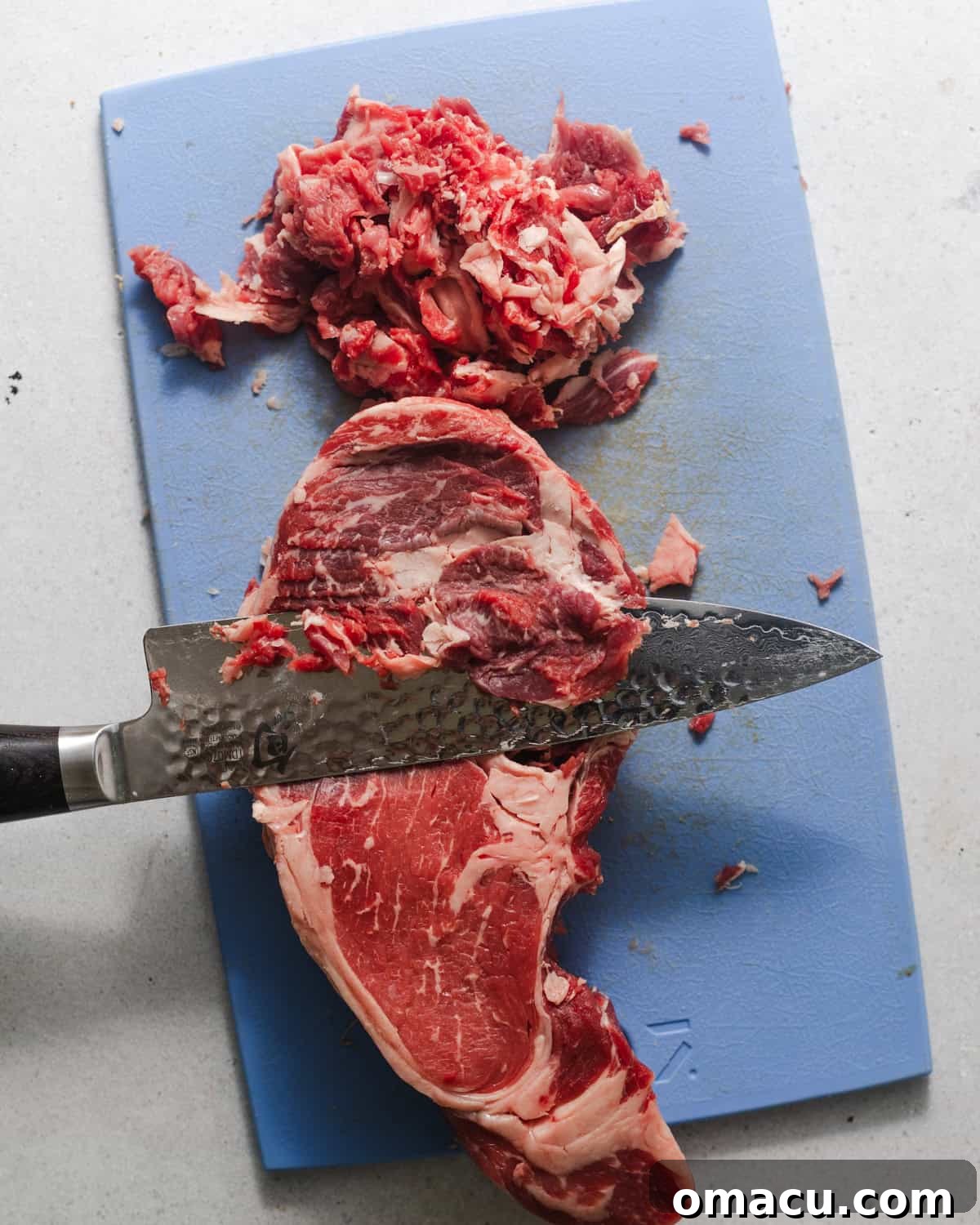 A sharp knife thinly slicing a ribeye steak on a cutting board, illustrating the critical first step for a perfect Philly cheesesteak.