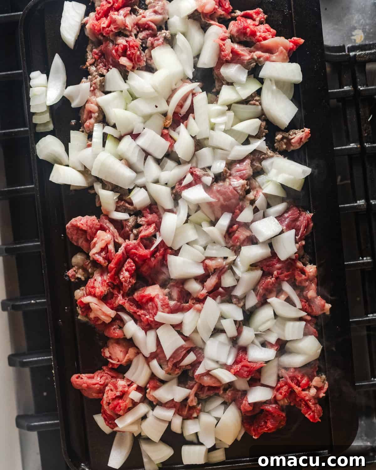 Ribeye steak and onions sizzling on a hot griddle, capturing the cooking process.