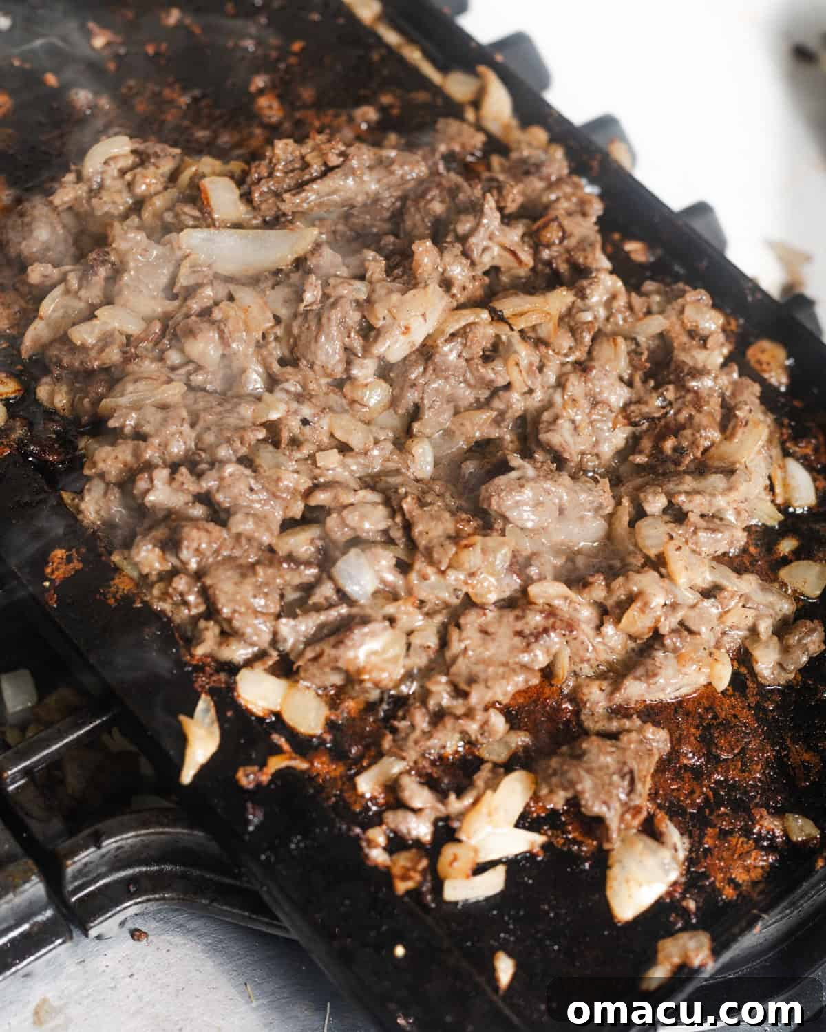 The cooked cheesesteak filling, featuring chopped steak and caramelized onions, ready for the cheese, on a griddle.