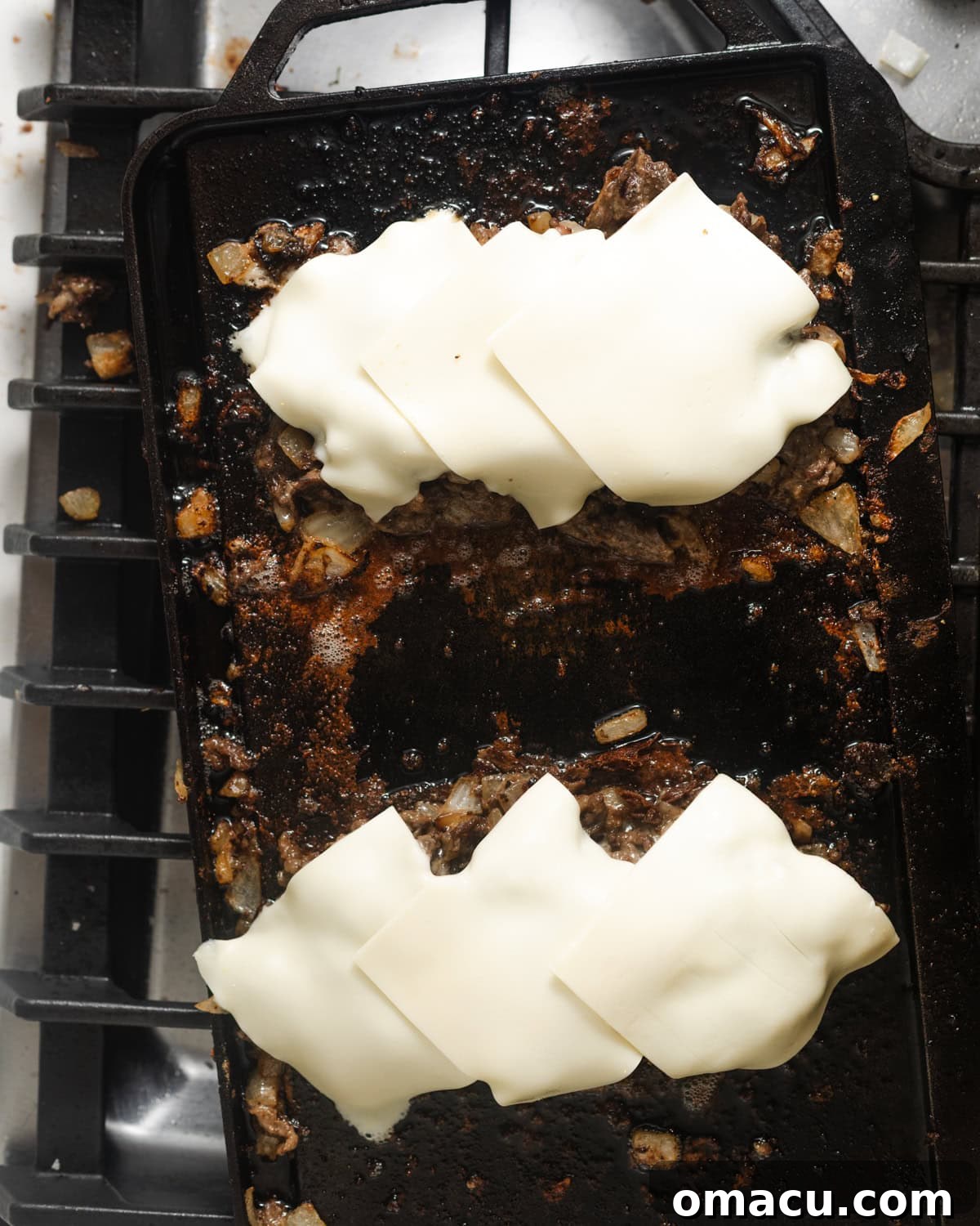 Two generous stacks of cheesesteak filling, each crowned with multiple slices of American cheese, ready to melt.