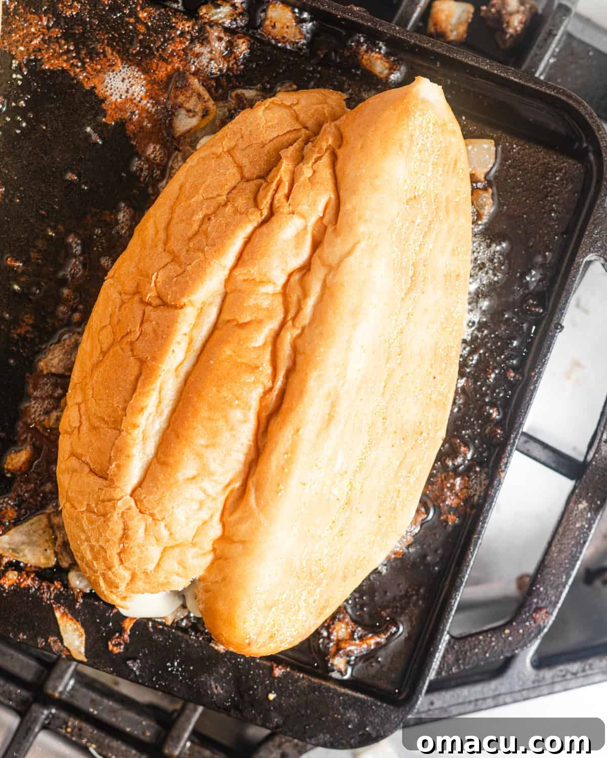 A classic hoagie roll placed upside down on top of the melted cheesesteak filling, preparing for assembly.