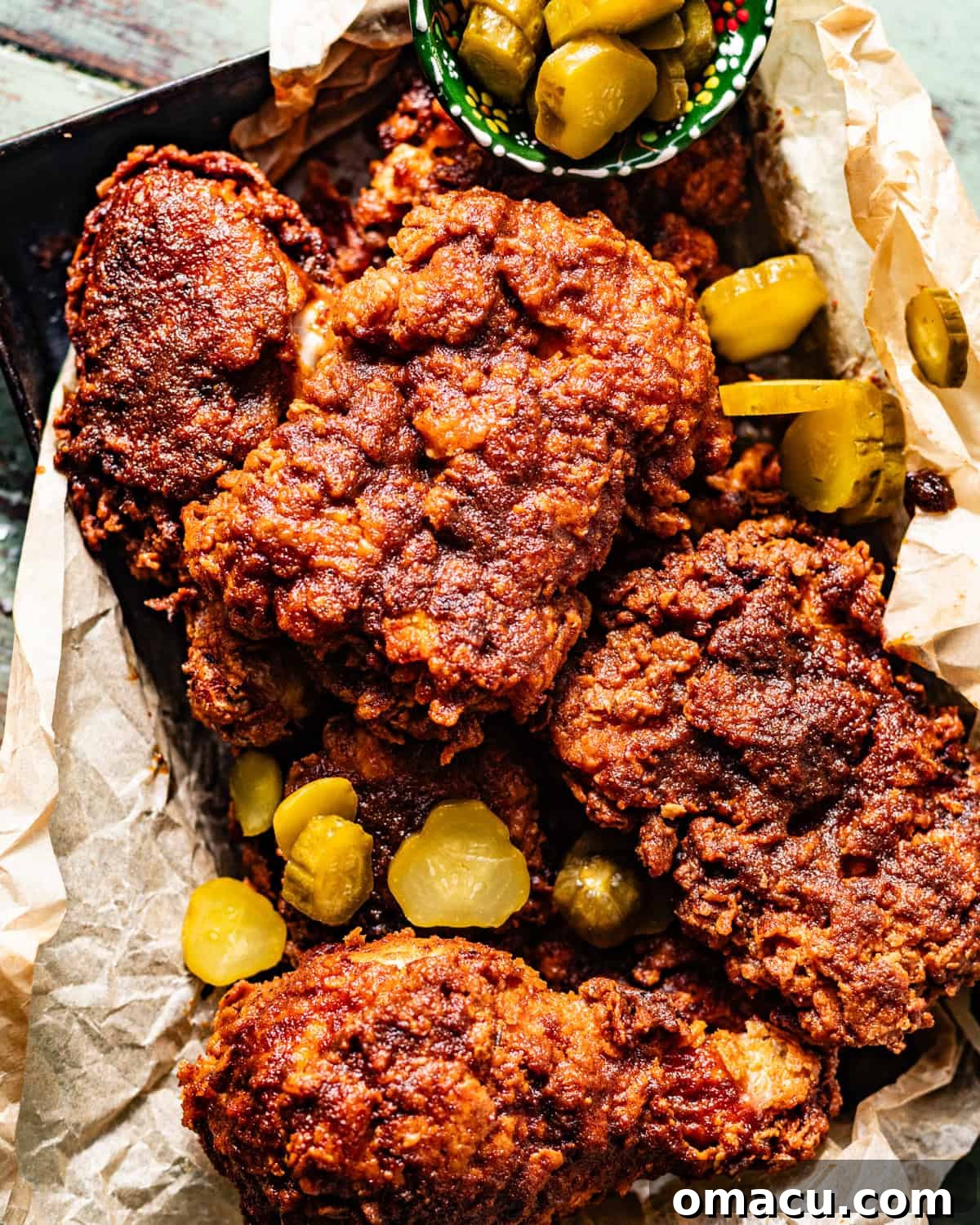 A basket of perfectly golden Nashville Hot Chicken, nestled on white bread with a side of sliced pickles, ready to be enjoyed.