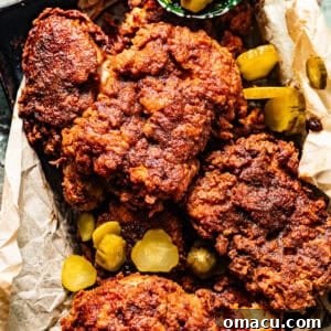 A basket of perfectly golden Nashville Hot Chicken, nestled on white bread with a side of sliced pickles, ready to be enjoyed.