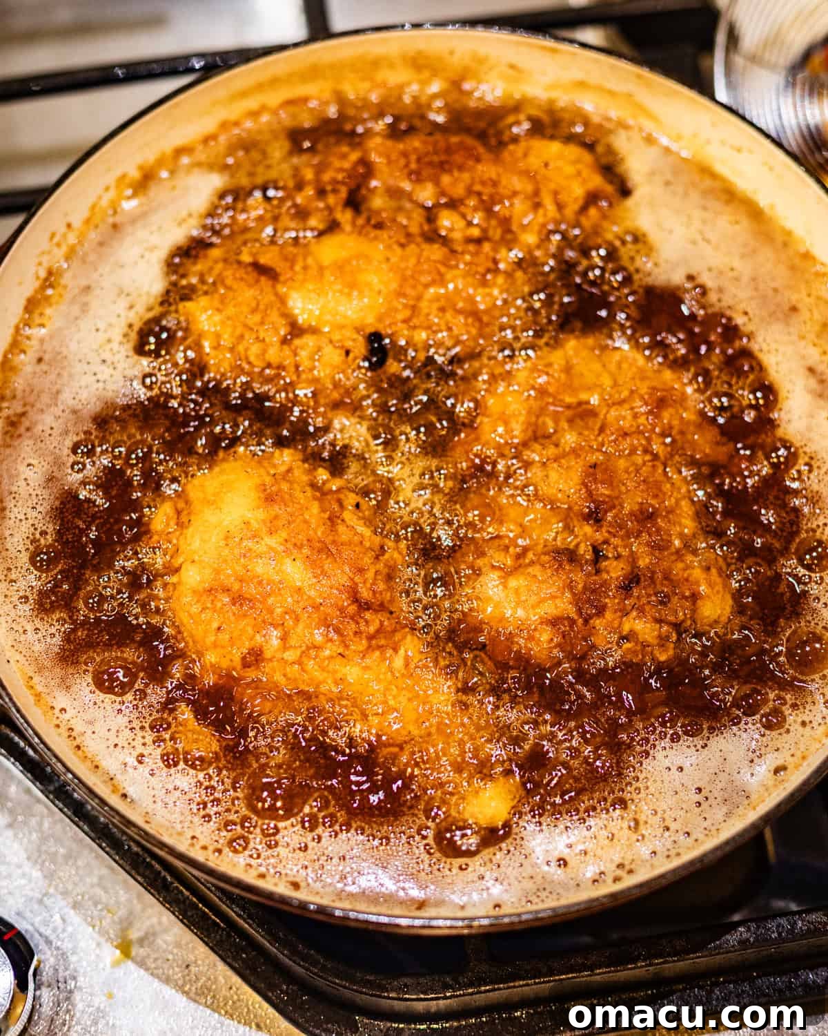 Golden-brown chicken pieces sizzling in hot oil within a deep pot, showing the frying process in action.