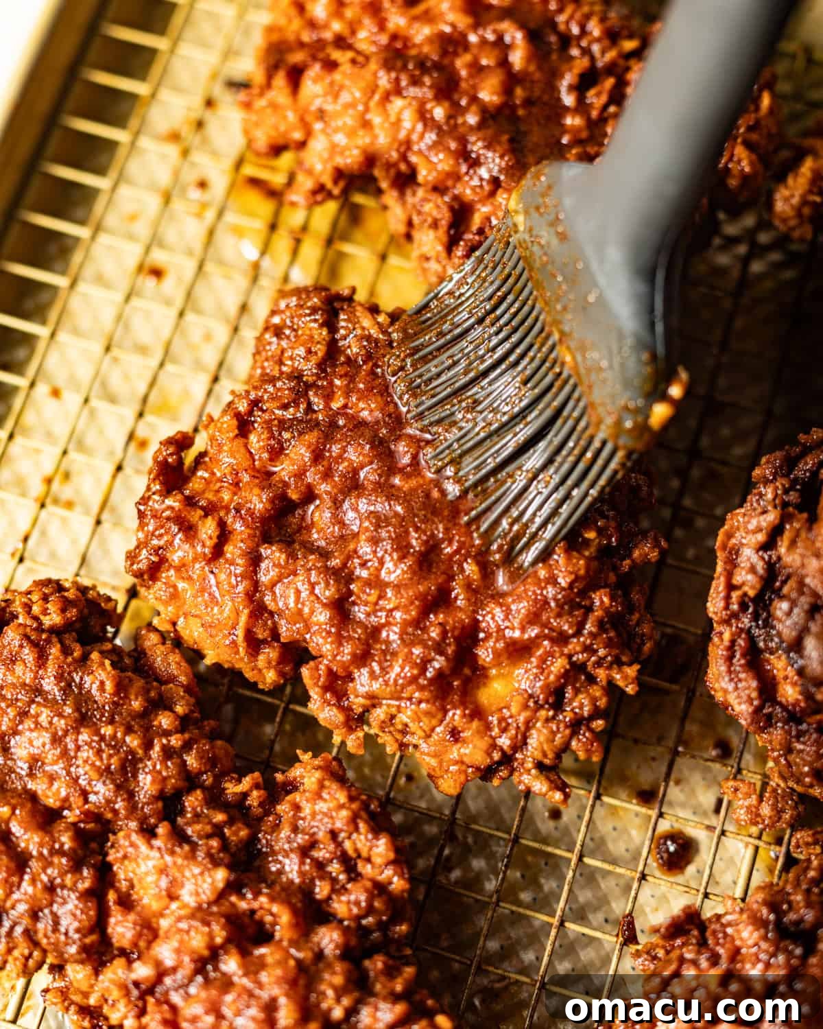 A BBQ brush expertly coating a piece of Nashville Hot Chicken with the glistening, fiery sauce, highlighting its vibrant color.