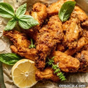 Crispy lemon pepper wings on a piece of parchment paper with lemons and fresh basil.