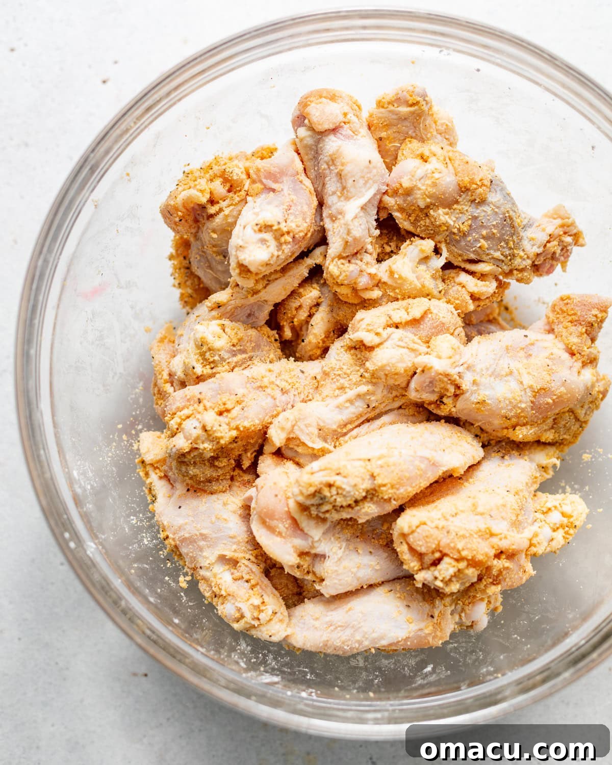 Chicken wings coated in a vibrant mix of cornstarch, various seasonings, mustard, baking powder, and olive oil, all ready for marination in a large mixing bowl.