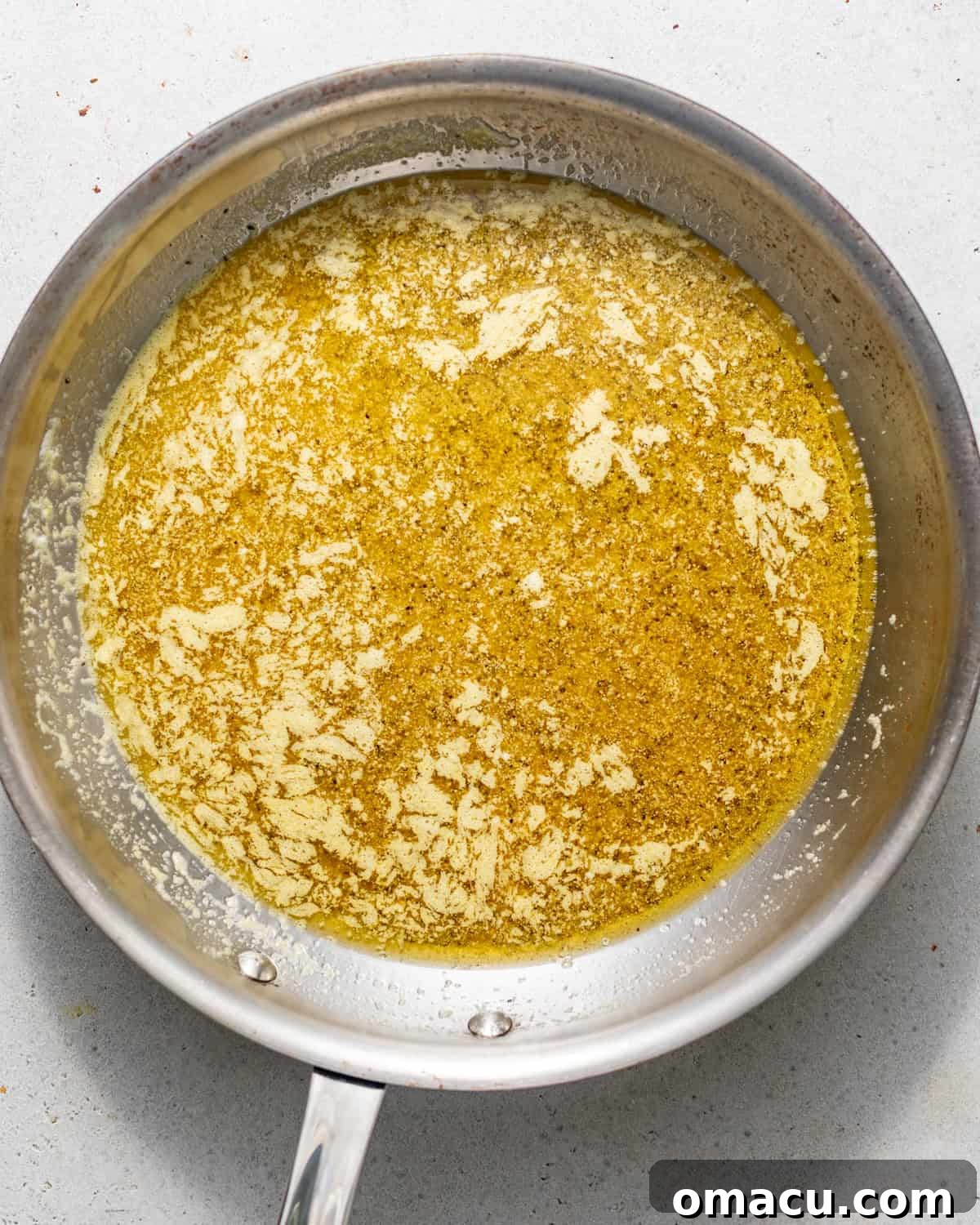 A small saucepan filled with the simmering lemon pepper sauce, showing the rich, golden-yellow hue of melted butter, lemon juice, zest, seasonings, and honey, ready to coat the wings.