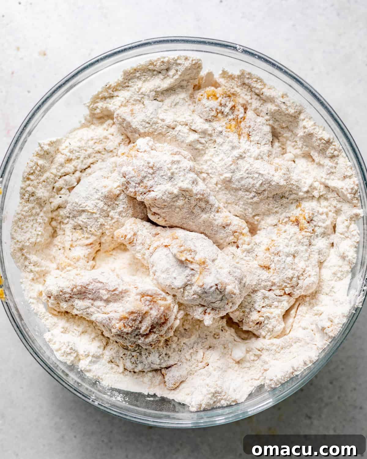 Marinated chicken wings generously coated in the flour dredge, ready for frying, resting in a bowl, showcasing the even and thick breading.
