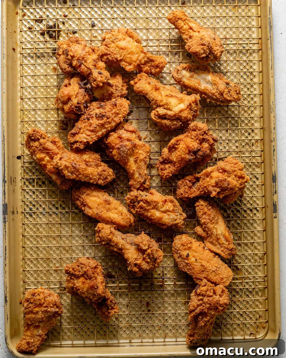 Freshly fried lemon pepper wings, golden brown and exceptionally crispy, draining excess oil on a wire rack, ready for the final sauce toss.