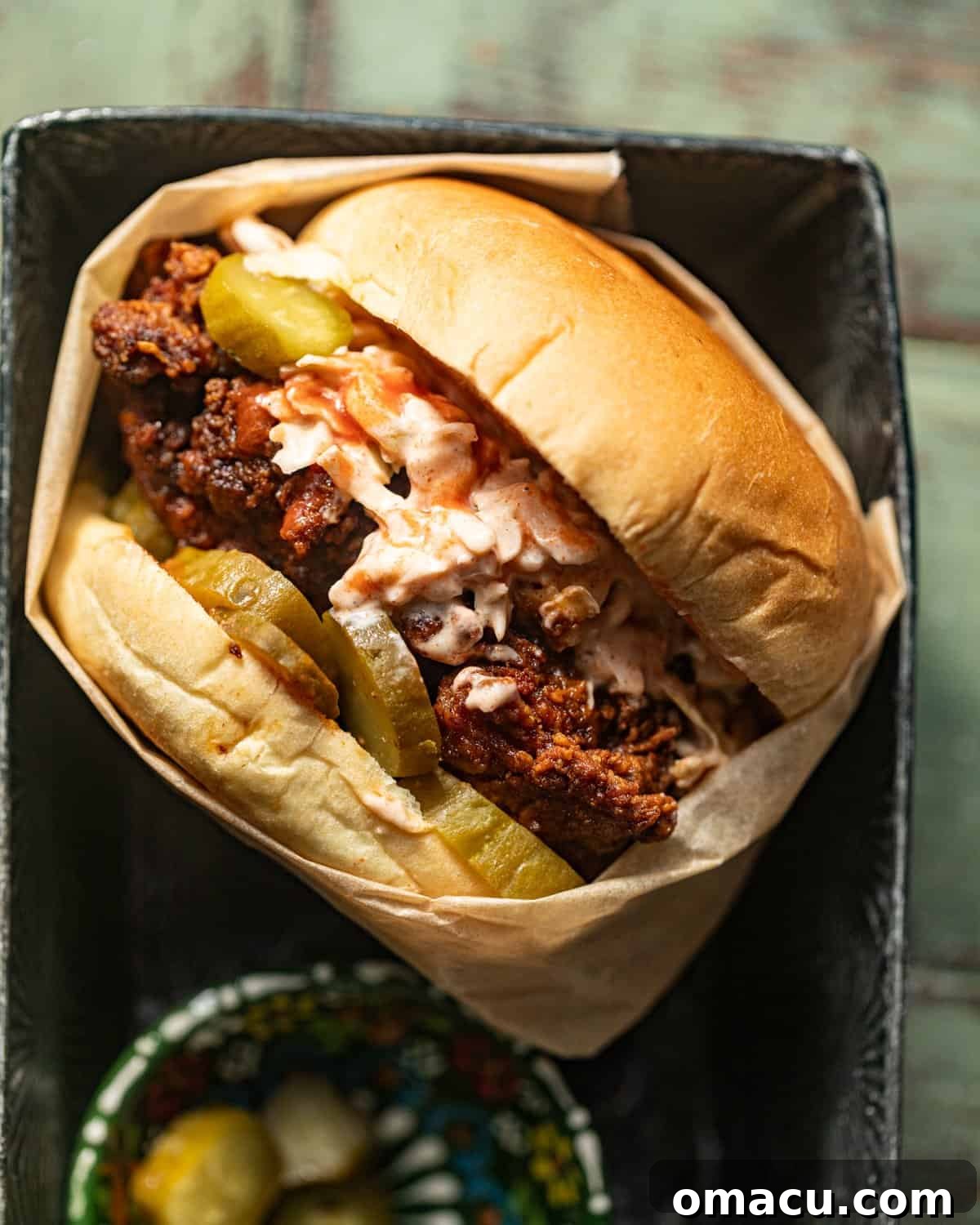nashville hot chicken sandwich wrapped in parchment paper on a serving basket.