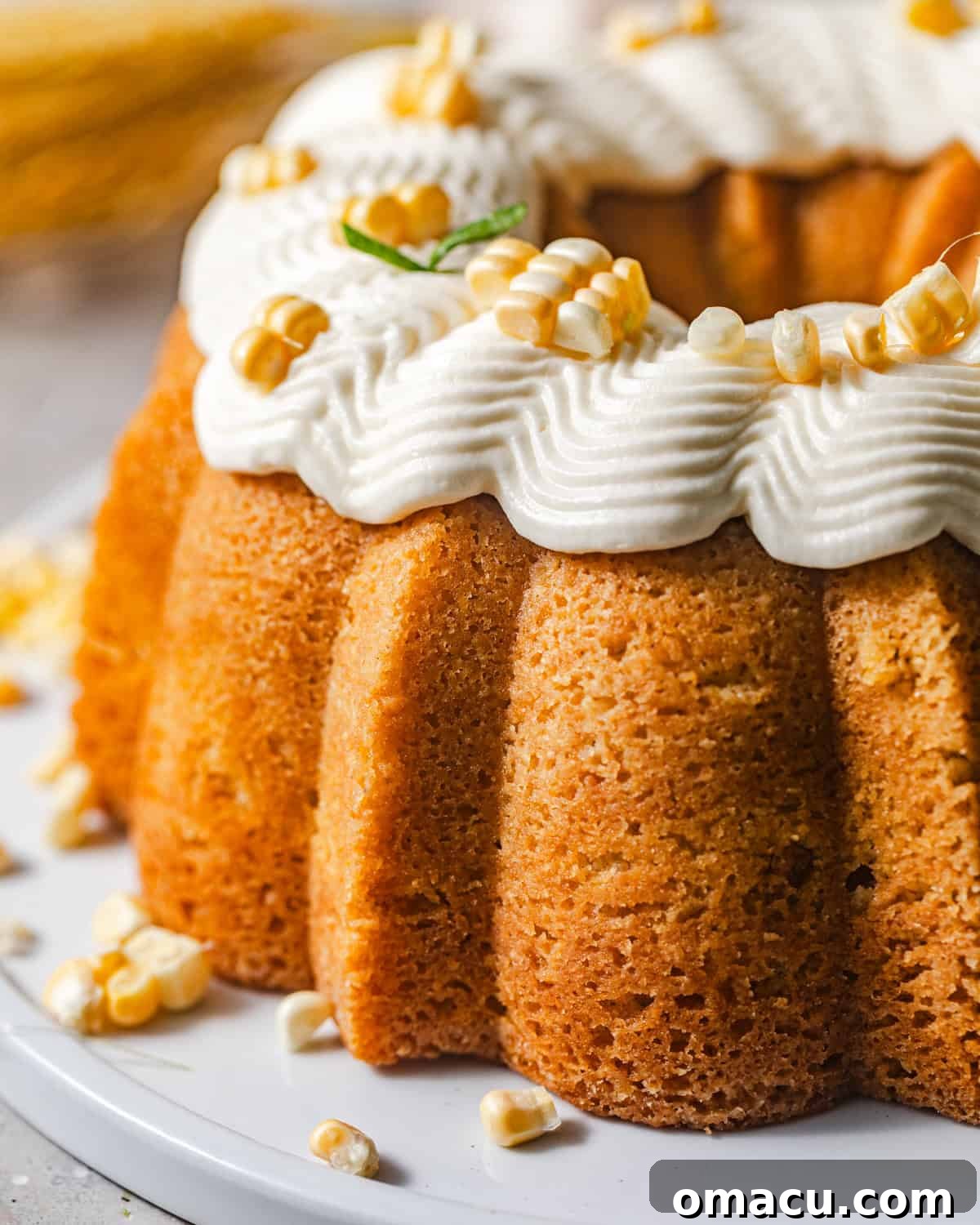 up close photo of corn pound cake on a white plate topped with fresh corn and honey buttercream.