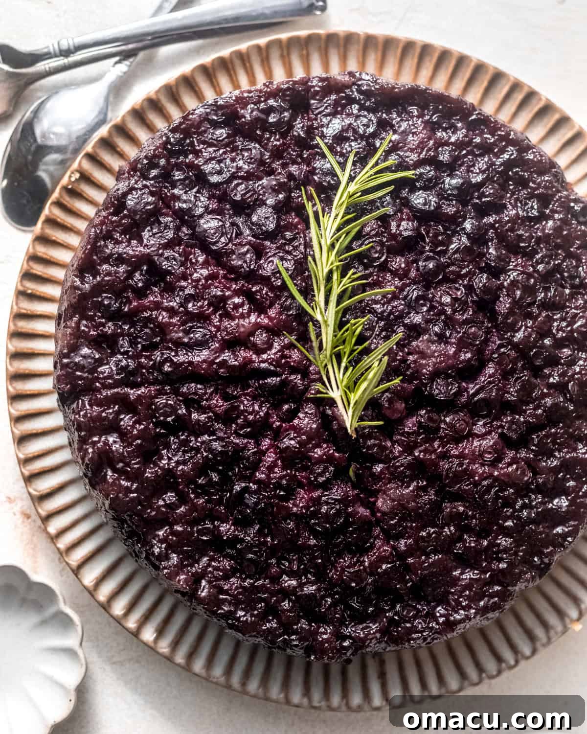 An overhead shot of a freshly baked blueberry upside down cake, garnished with a sprig of fresh rosemary, highlighting its beautiful, golden-brown crust.