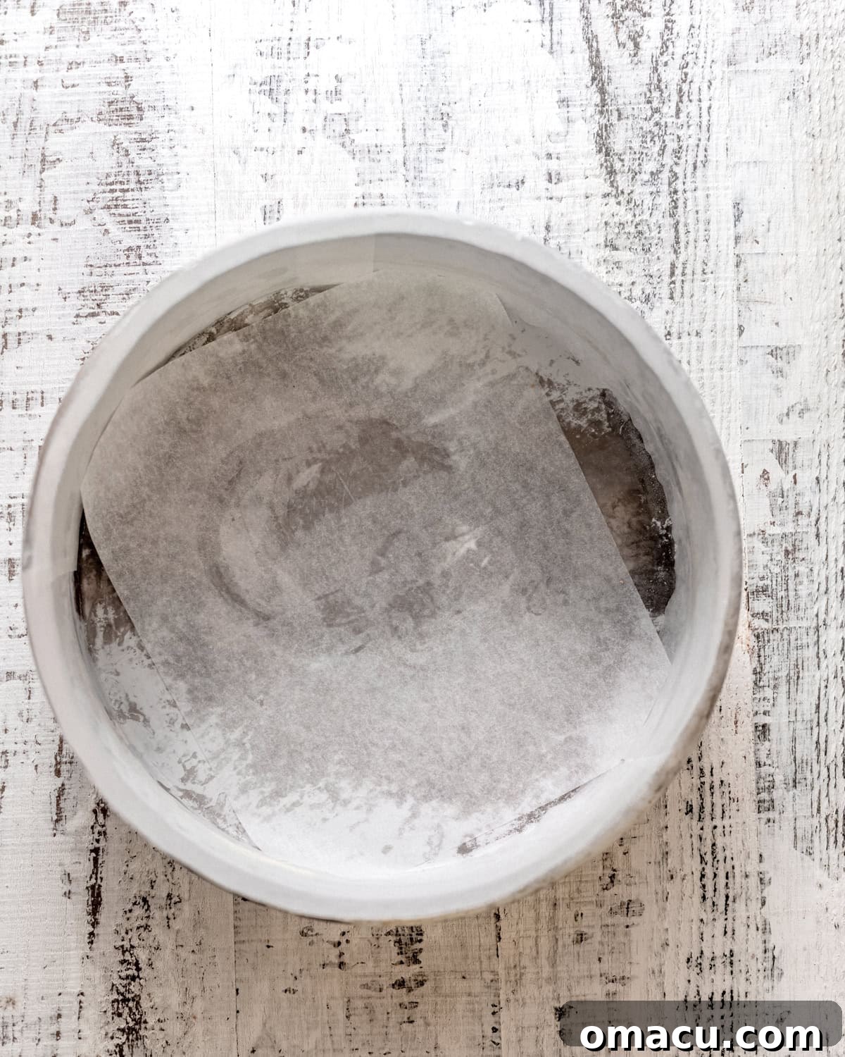 A 9 by 2 inch cake pan perfectly lined with parchment paper, brushed with butter, ready for the blueberry topping.