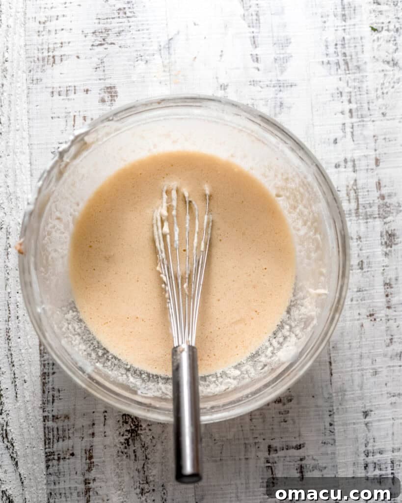 Wet ingredients, including butter, oil, lemon zest, and sugar, thoroughly mixed together in a bowl, appearing pale and fluffy.
