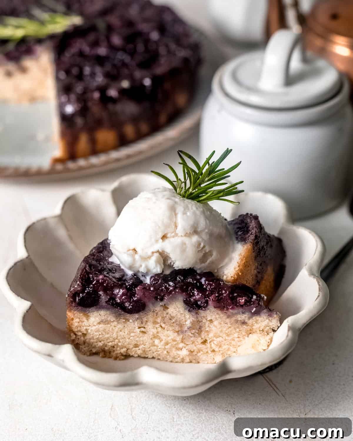 A warm slice of blueberry upside down cake served in a bowl, topped with a scoop of melting vanilla ice cream.