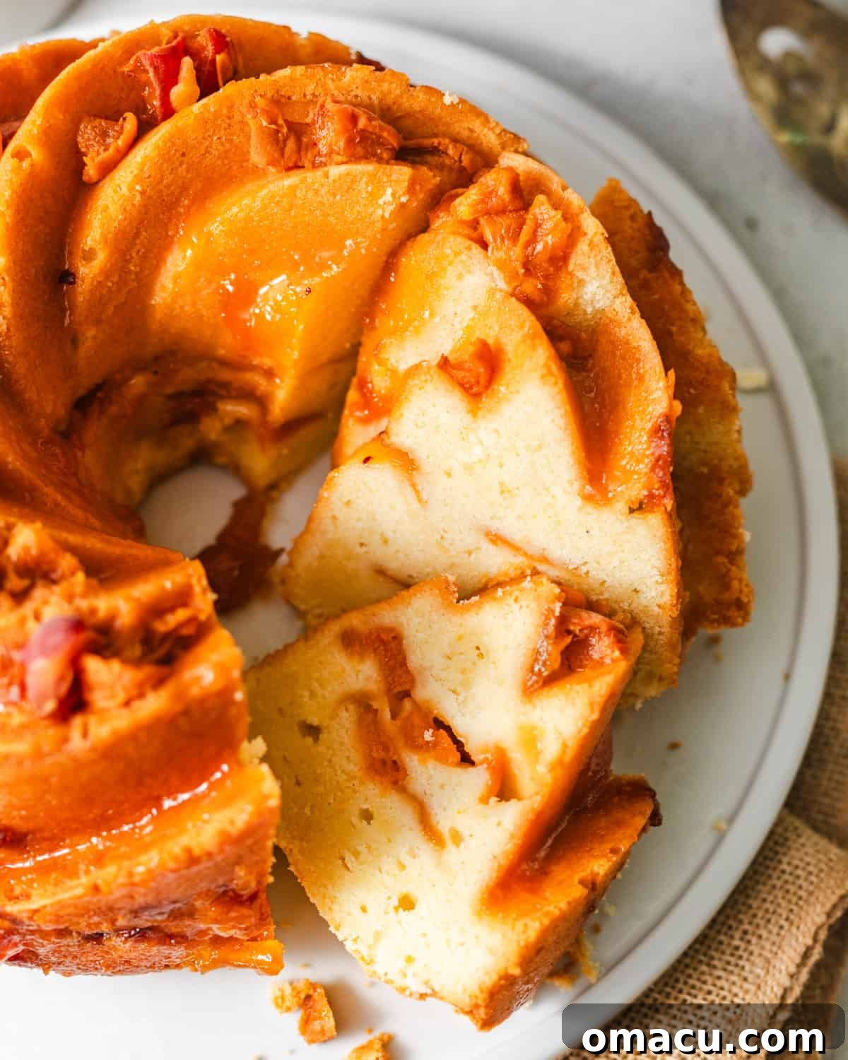 A generous slice of fresh apricot cake, revealing its moist crumb, golden crust, and the pockets of juicy apricots baked within. The slice sits on a white plate, ready to be enjoyed.