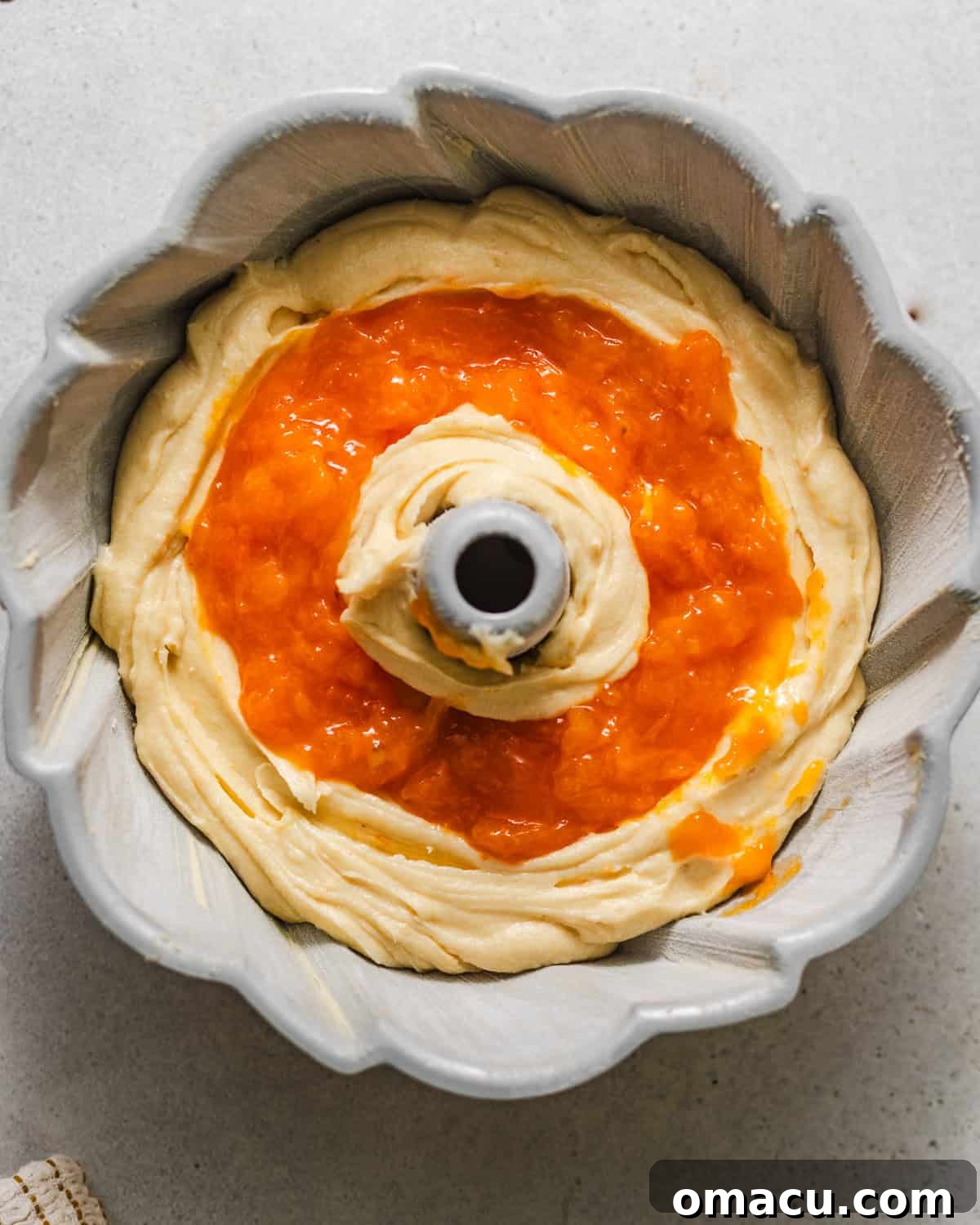 The apricot filling strategically placed in the center of the cake batter within the bundt pan, ready to be covered with the remaining batter for baking, showing the fruit swirl technique.