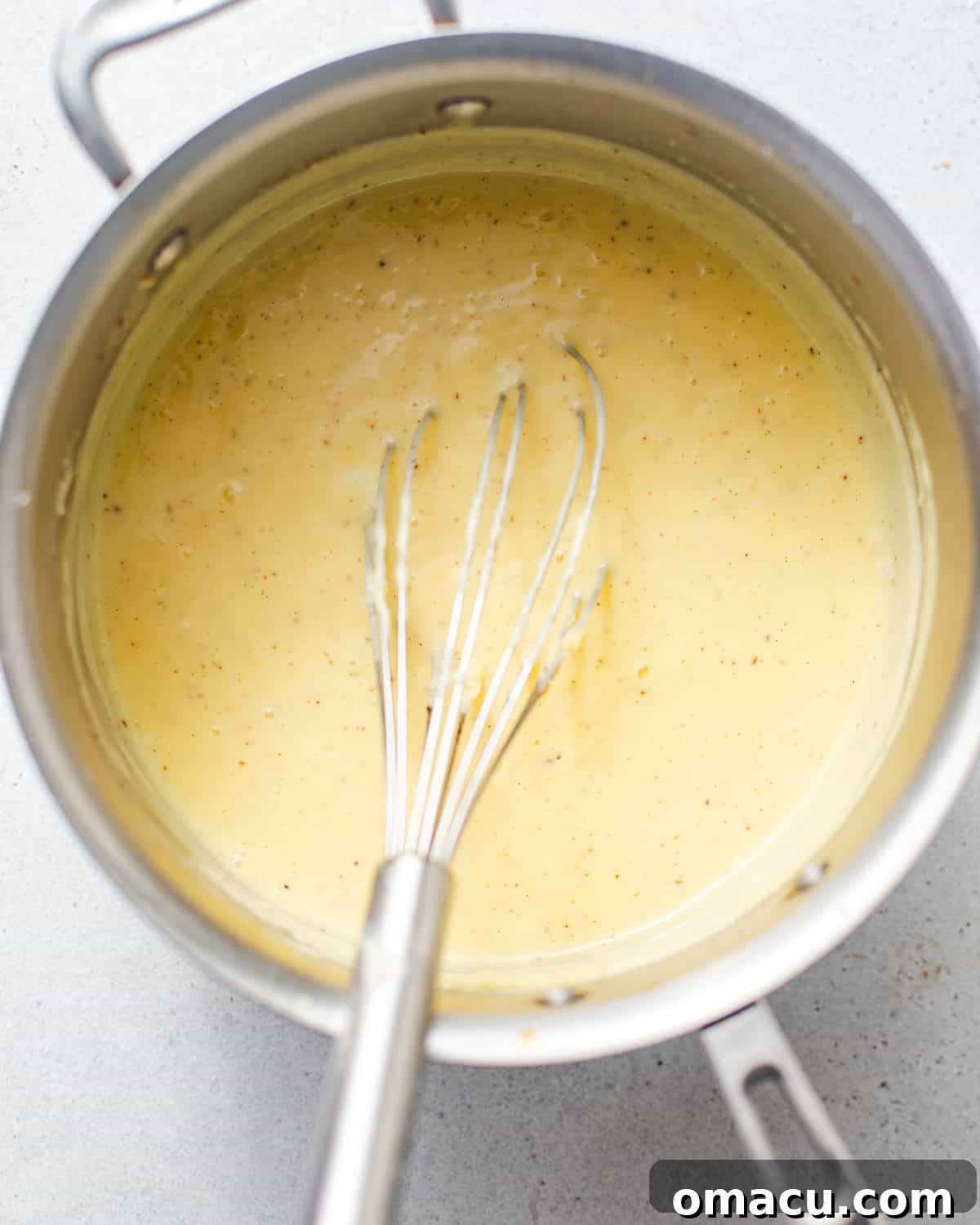 A saucepan on the stove, containing the thickening vanilla custard, being constantly whisked to achieve a smooth consistency.
