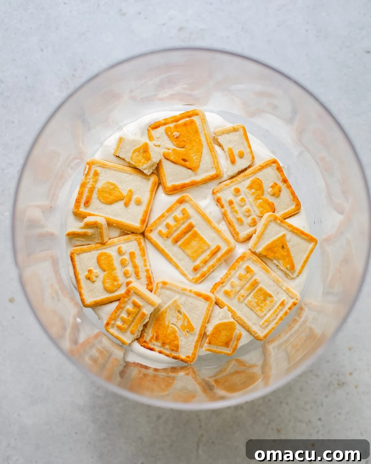 An overhead view of the initial layers of whipped cream and Chessman cookies being placed into a trifle bowl for the banana pudding.