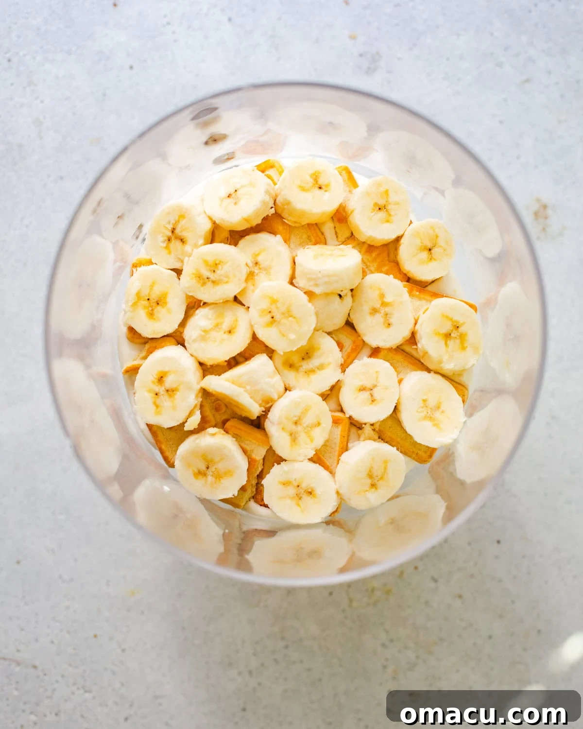 Slices of fresh bananas arranged neatly on top of the cookie layer in a trifle bowl, forming the next step in the pudding assembly.