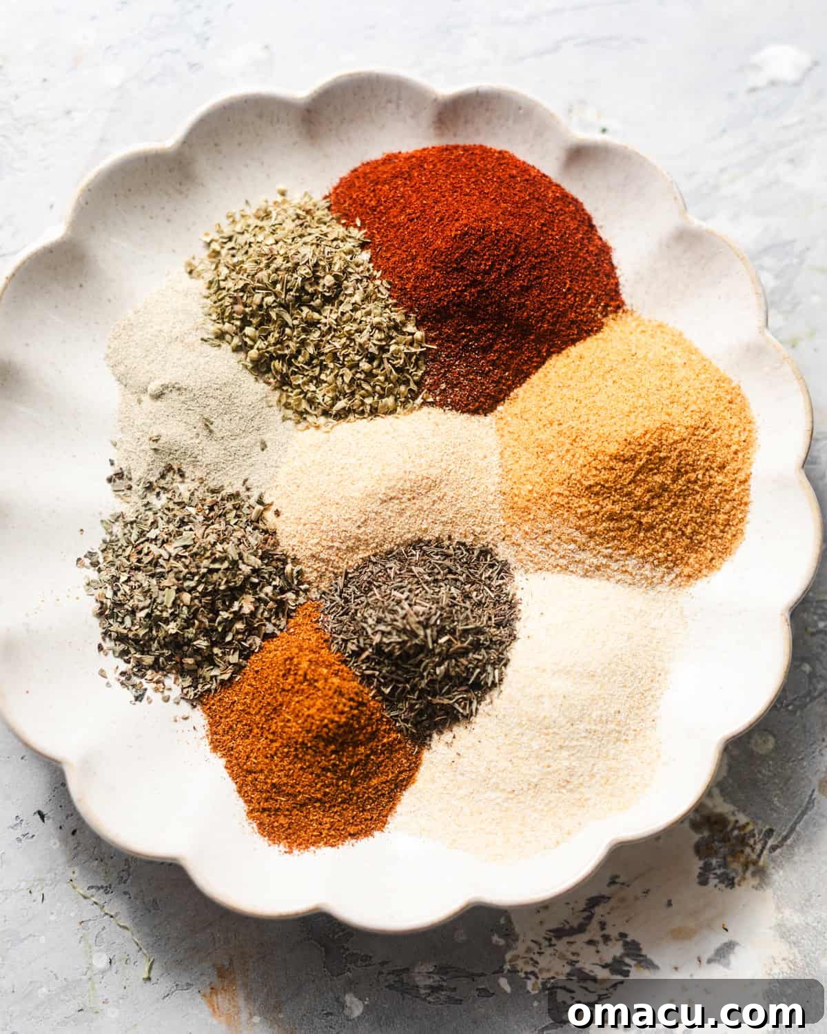 Collection of spices laid out: smoked paprika, seasoned salt, garlic powder, onion powder, oregano, basil, black pepper, thyme, white pepper, and cayenne pepper.